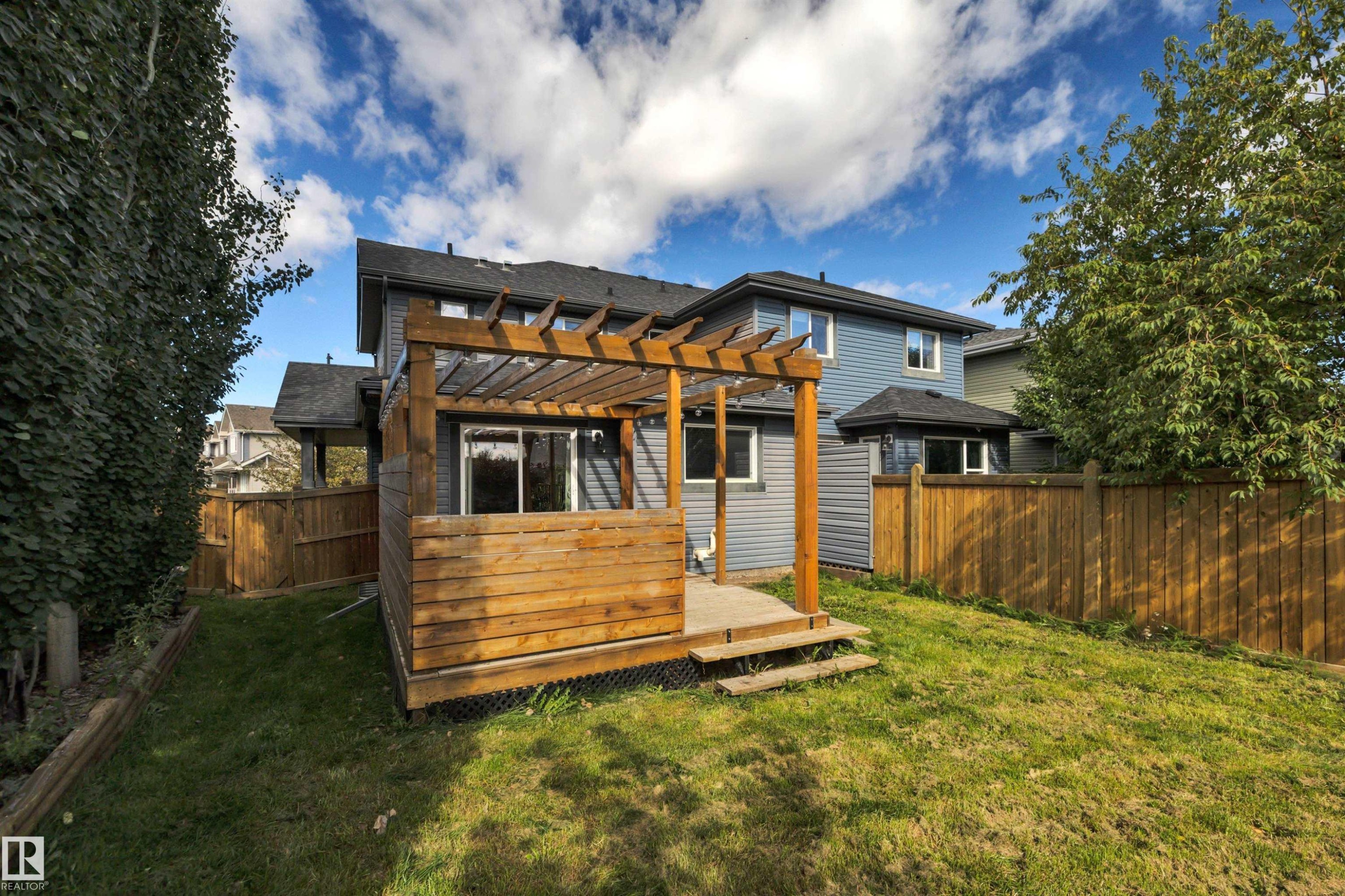 Two-story residence with blue siding, wood pergola, raised wood deck, and a fenced backyard with a large grass area - 12903 205 Street Nw, Edmonton, AB