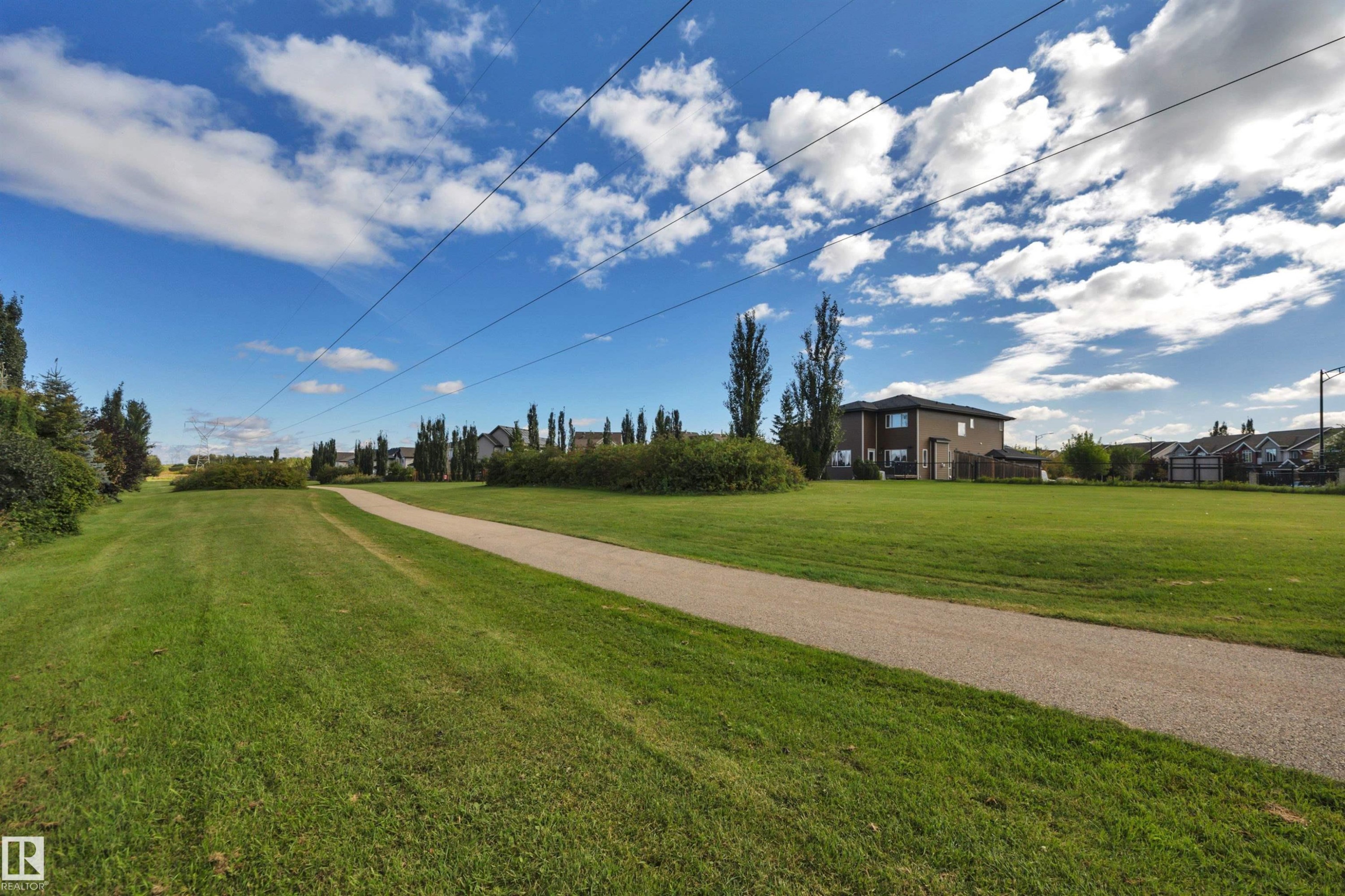 Expansive green space with a paved pathway, bordered by mature landscaping and residential properties - 12903 205 Street Nw, Edmonton, AB