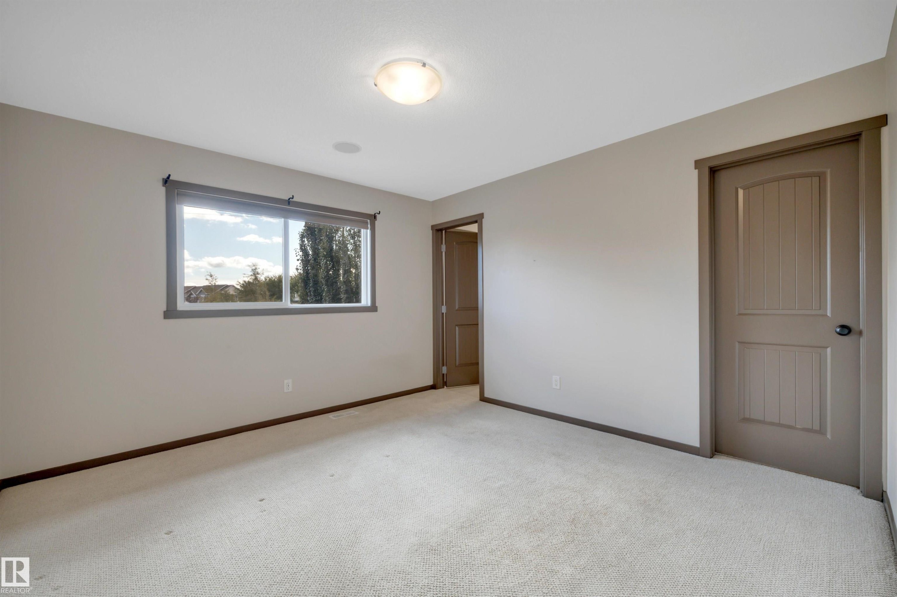 Neutral-toned carpet flooring, a window offering natural light, and a flush-mount ceiling light fixture - 12903 205 Street Nw, Edmonton, AB