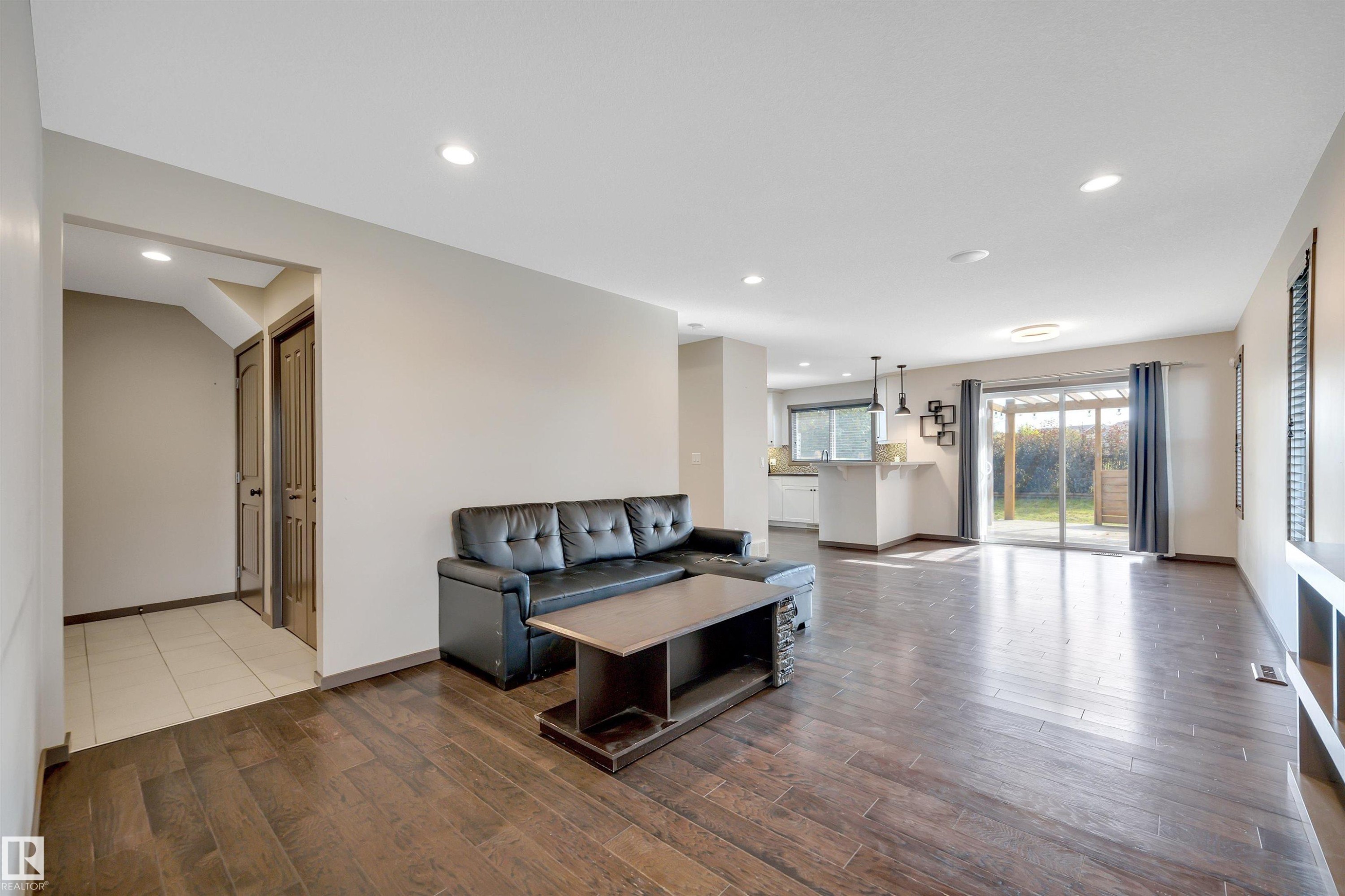 Expansive living area featuring rich wood-finish flooring, recessed lighting, and a sliding glass door to the exterior - 12903 205 Street Nw, Edmonton, AB