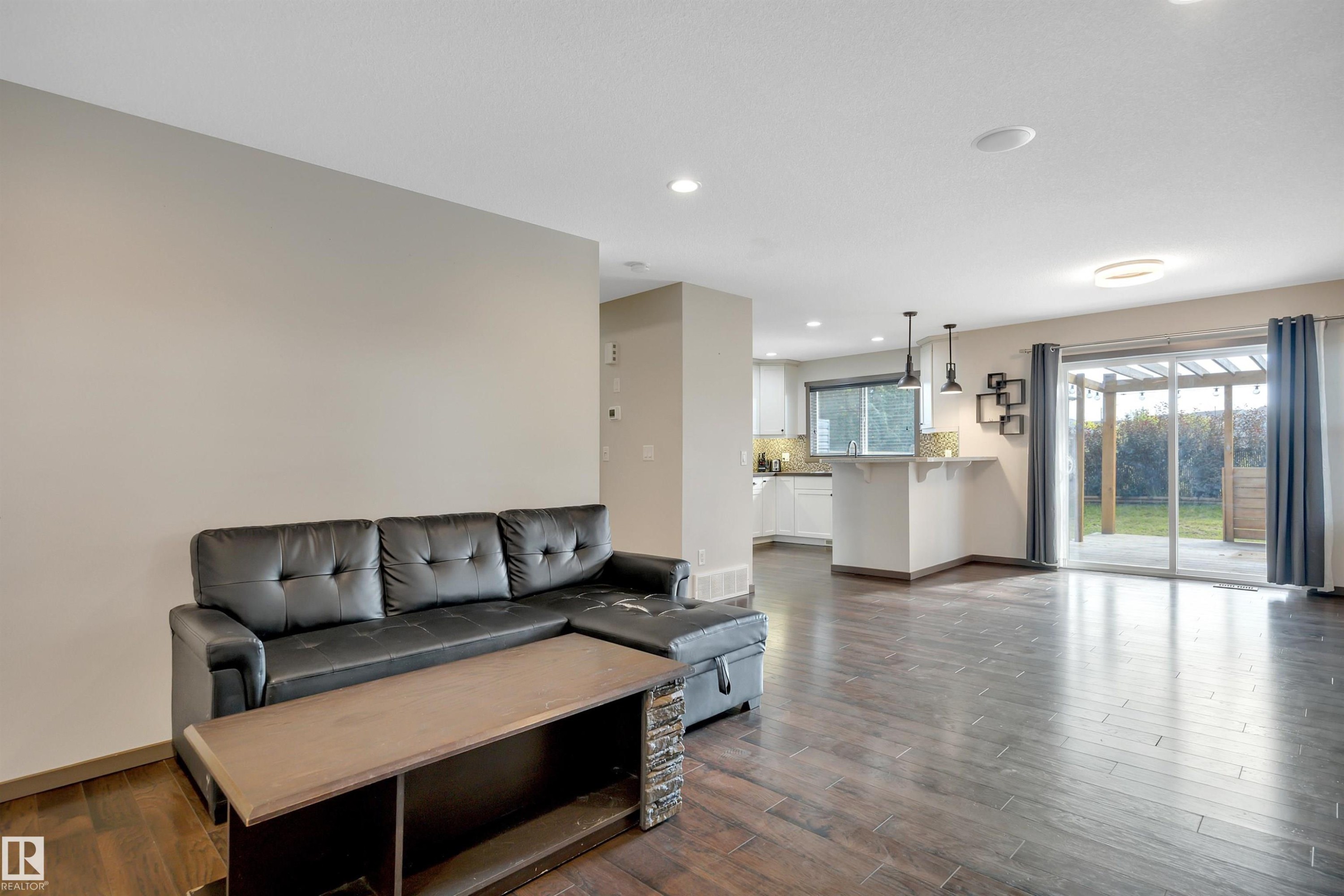 Recessed lighting, wood-finish flooring, sliding glass door, white cabinetry, and a kitchen island with pendant lighting - 12903 205 Street Nw, Edmonton, AB
