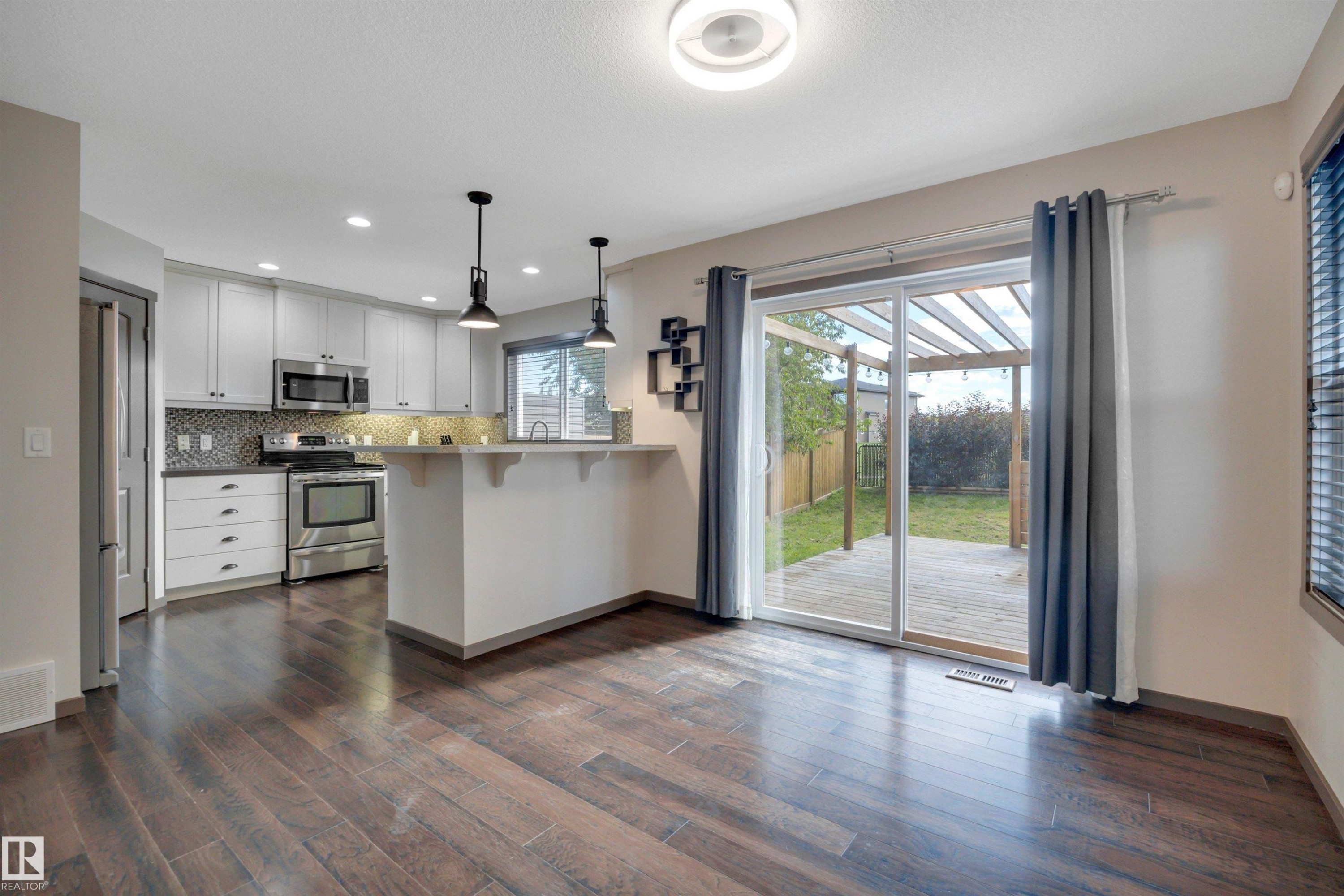 Wood-finish flooring throughout, kitchen with white cabinetry, stainless steel appliances, and a tiled backsplash - 12903 205 Street Nw, Edmonton, AB