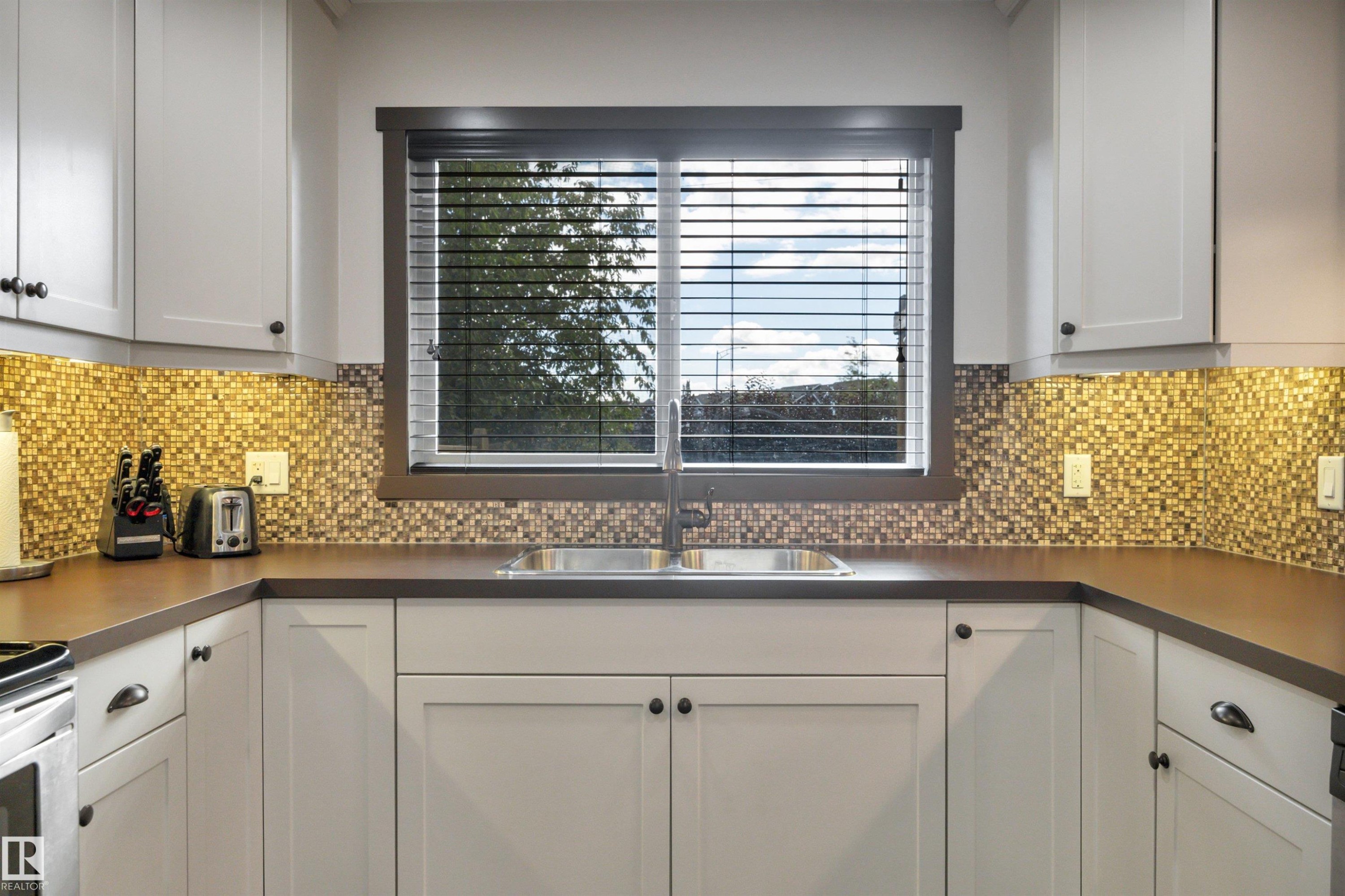 White shaker-style cabinetry with dark hardware, mosaic tile backsplash, composite countertop, and double basin stainless steel sink - 12903 205 Street Nw, Edmonton, AB