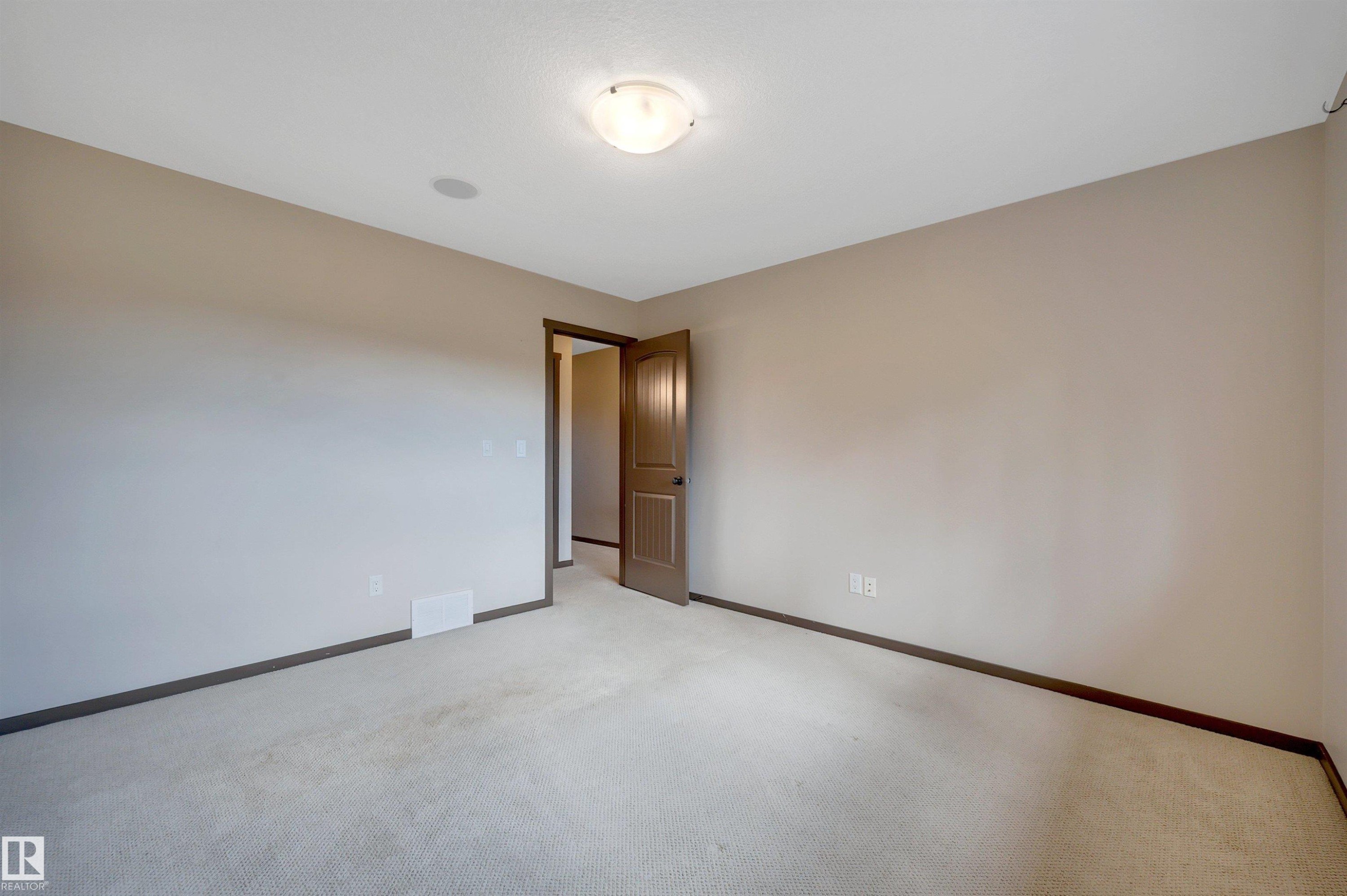 Neutral wall paint, light-toned carpeting, wood-finish interior door, flush-mount ceiling light fixture, and ceiling-mounted speaker - 12903 205 Street Nw, Edmonton, AB