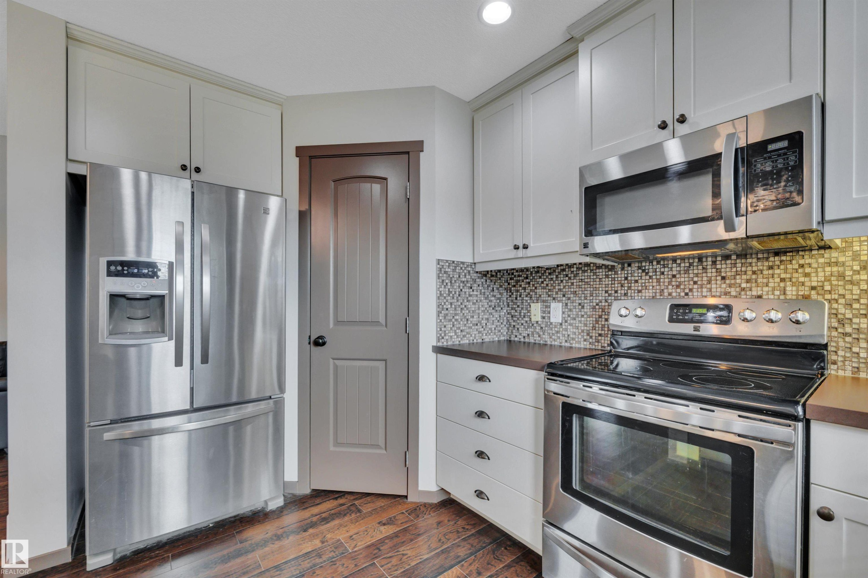 Stainless steel appliance suite, light-toned cabinetry, mosaic tile backsplash, wood-finish flooring, and dark countertops - 12903 205 Street Nw, Edmonton, AB