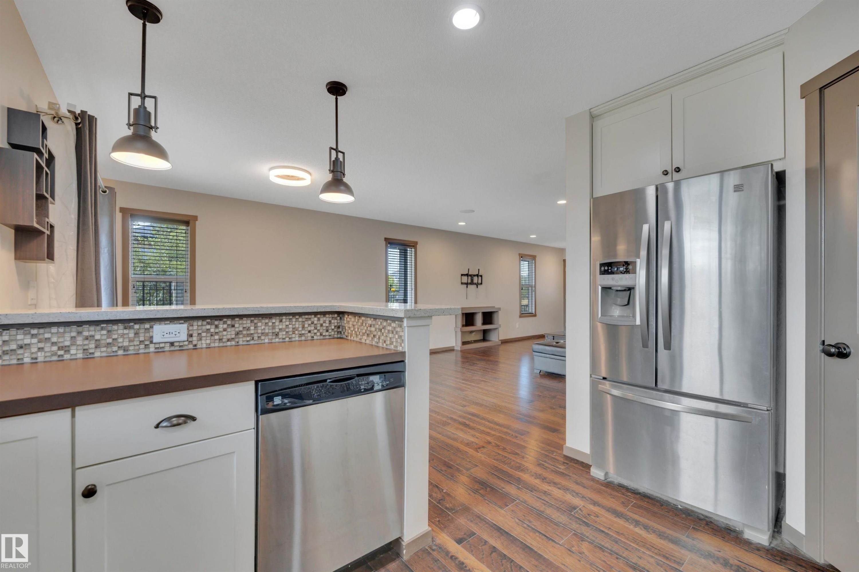 Stainless steel appliances, wood-finish flooring, white cabinetry, and multi-toned tile backsplash - 12903 205 Street Nw, Edmonton, AB