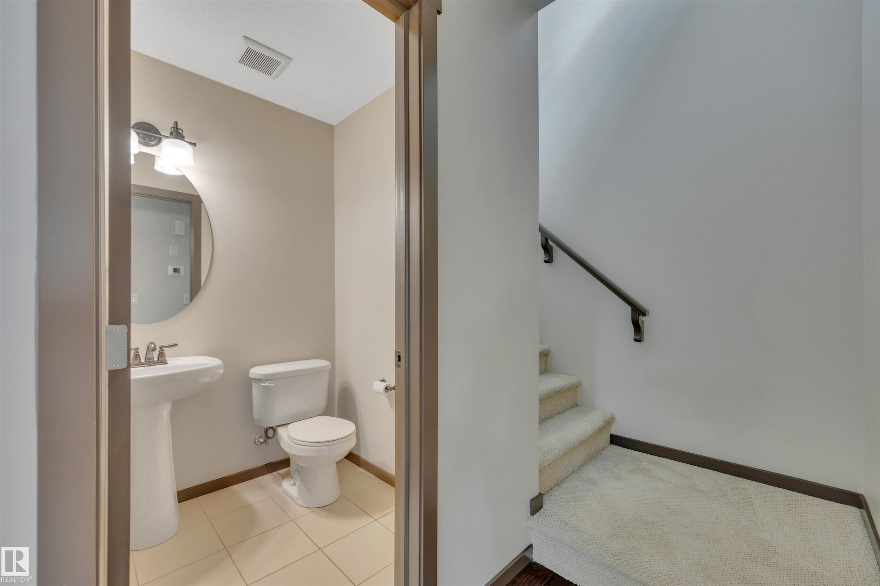Powder room with pedestal sink, round mirror, and tile flooring - 12903 205 Street Nw, Edmonton, AB