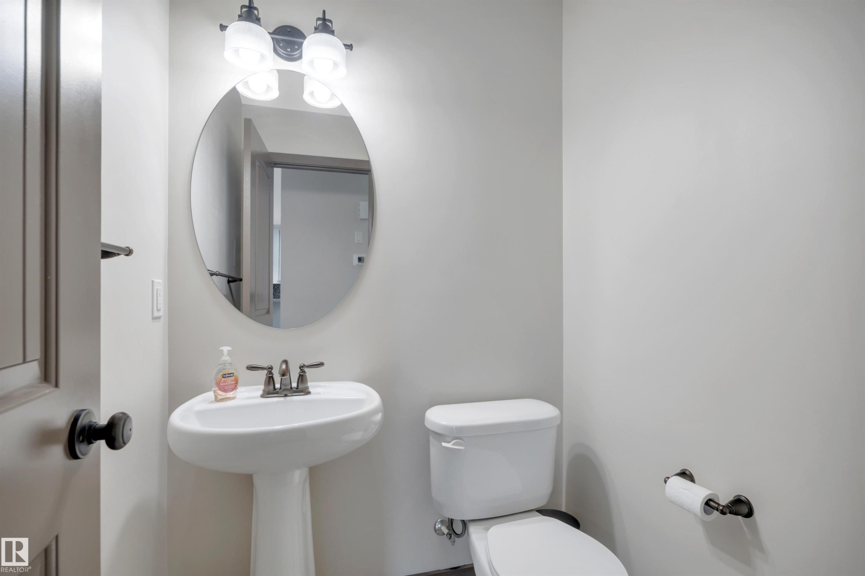 Pedestal sink with a wall-mounted mirror, two-light fixture, and a white toilet - 12903 205 Street Nw, Edmonton, AB