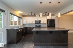 Kitchen featuring dark wood-finish flooring, two-tone cabinetry, built-in appliances, and a large island with pendant lighting - 