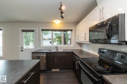 Modern kitchen featuring white upper cabinetry, dark lower cabinetry, stainless steel dishwasher, and black range with microwave - 