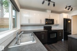 Modern kitchen featuring white upper cabinetry, dark lower cabinetry, dark countertops, and coordinating black appliances - 