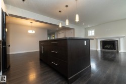 Dark wood-finish flooring throughout, central island with dark cabinetry and countertop, recessed lighting, and a fireplace with a decorative mantel and hearth - 