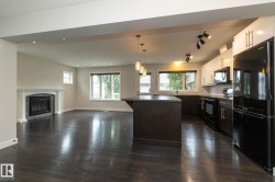 Dark wood-finish flooring throughout, modern kitchen with dark cabinetry and stainless steel appliances, central kitchen island with seating, fireplace with white mantel, and recessed lighting - 