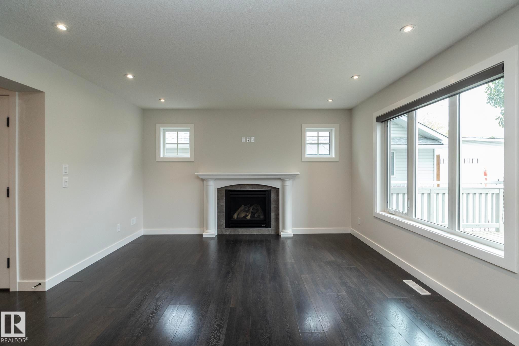Living area featuring dark wood-finish flooring, a white mantel fireplace with a dark stone surround, and multiple recessed ceiling lights - 53/55 Michigan Street, Devon, AB