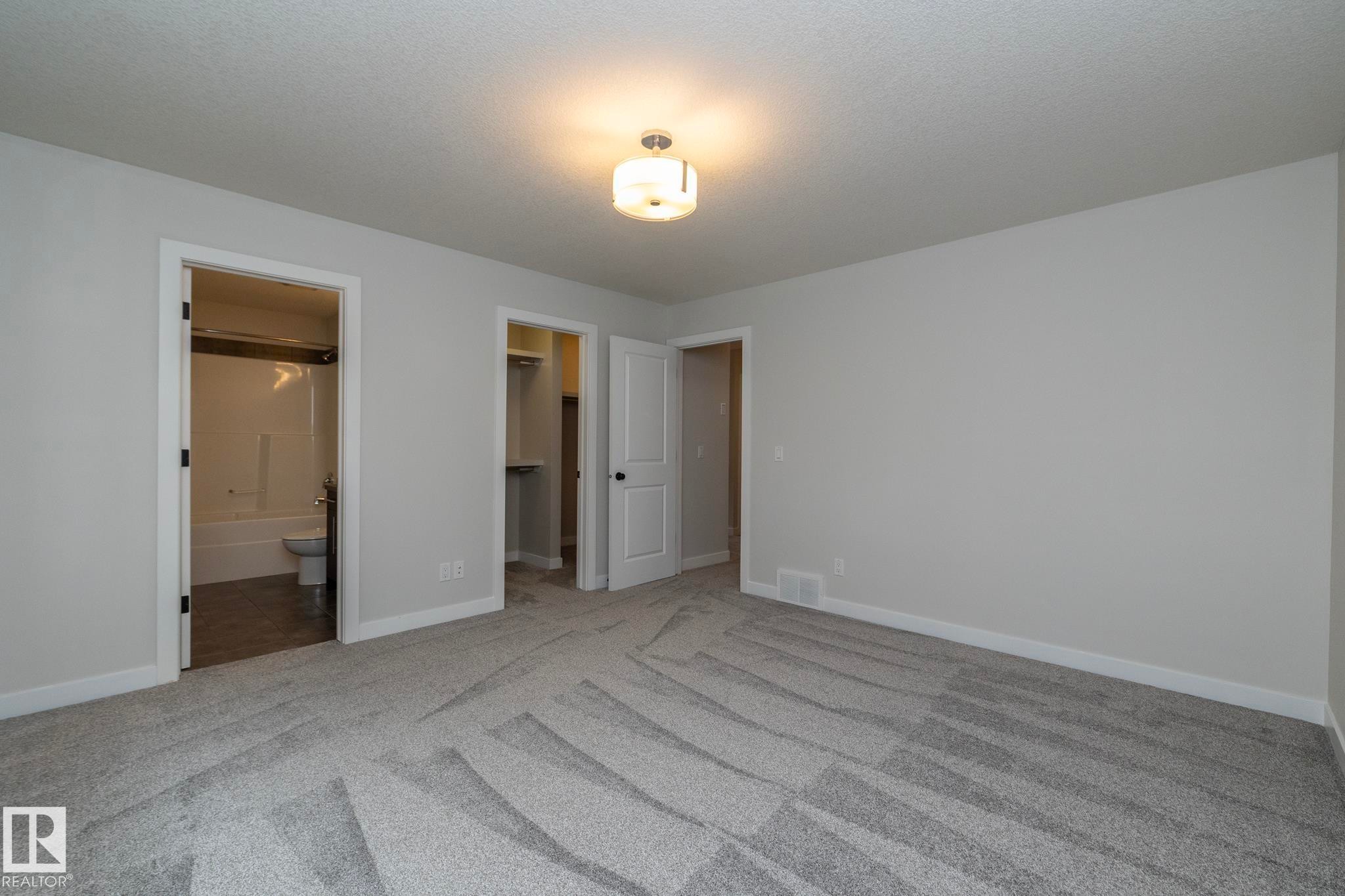 Neutral gray walls, patterned carpeting, flush mount light fixture, and an en-suite bathroom with a tub/shower combination - 53/55 Michigan Street, Devon, AB