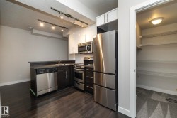 Kitchen featuring wood-finish flooring, track lighting, stainless steel appliances, and dark and white cabinetry - 