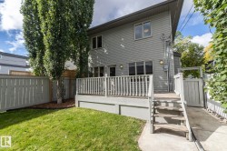 Grassed yard with mature trees, a multi-level deck, fenced perimeter, and exterior lighting - 
