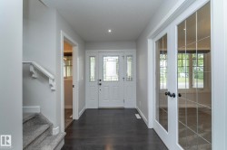 Entryway featuring a white door with decorative glass inserts, dark wood-finish flooring, recessed ceiling lighting, and a white staircase with carpeted treads - 