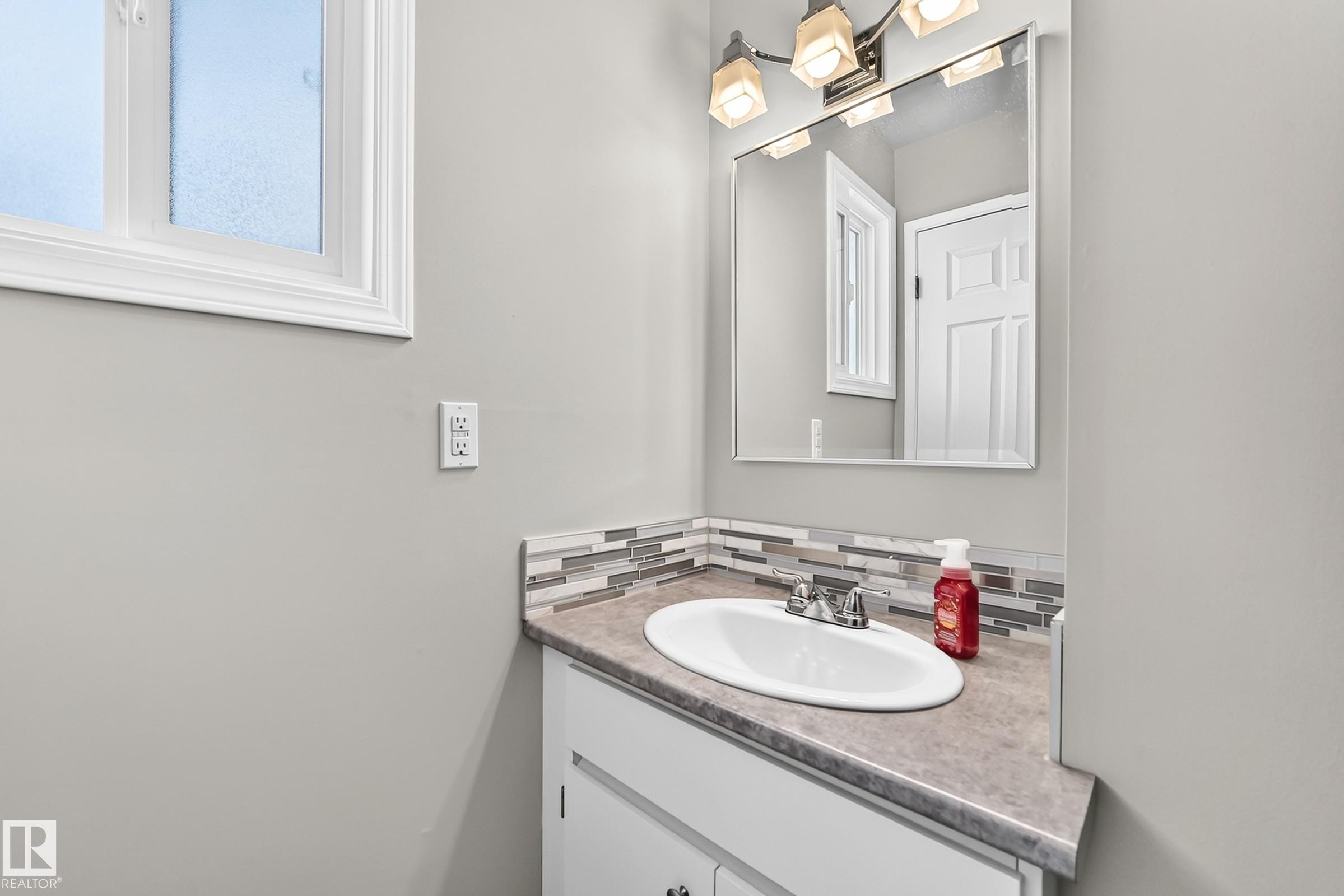 Frosted window with white trim, built-in vanity with under-sink storage, laminate countertop, oval undermount sink, and mosaic tile backsplash - 18146 81 Avenue Nw, Edmonton, AB