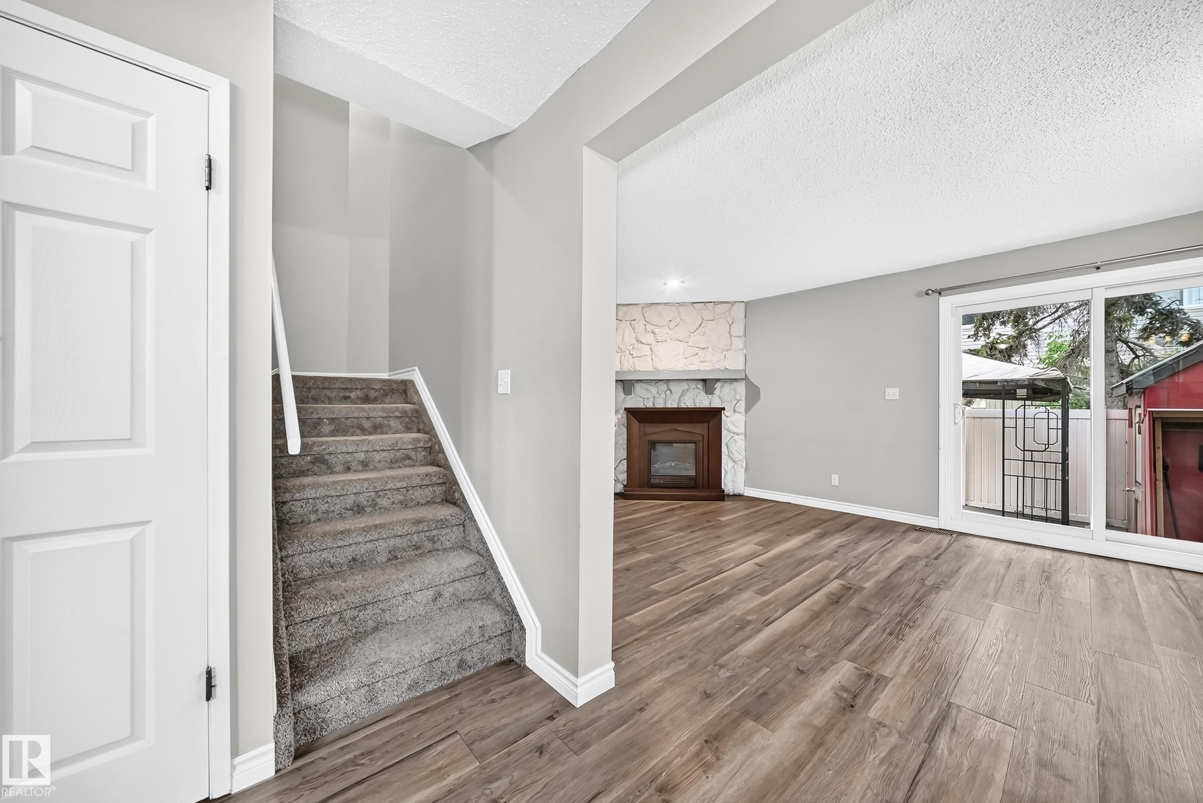 Living space featuring a stone-clad fireplace, wood-finish flooring, and sliding glass doors - 18146 81 Avenue Nw, Edmonton, AB