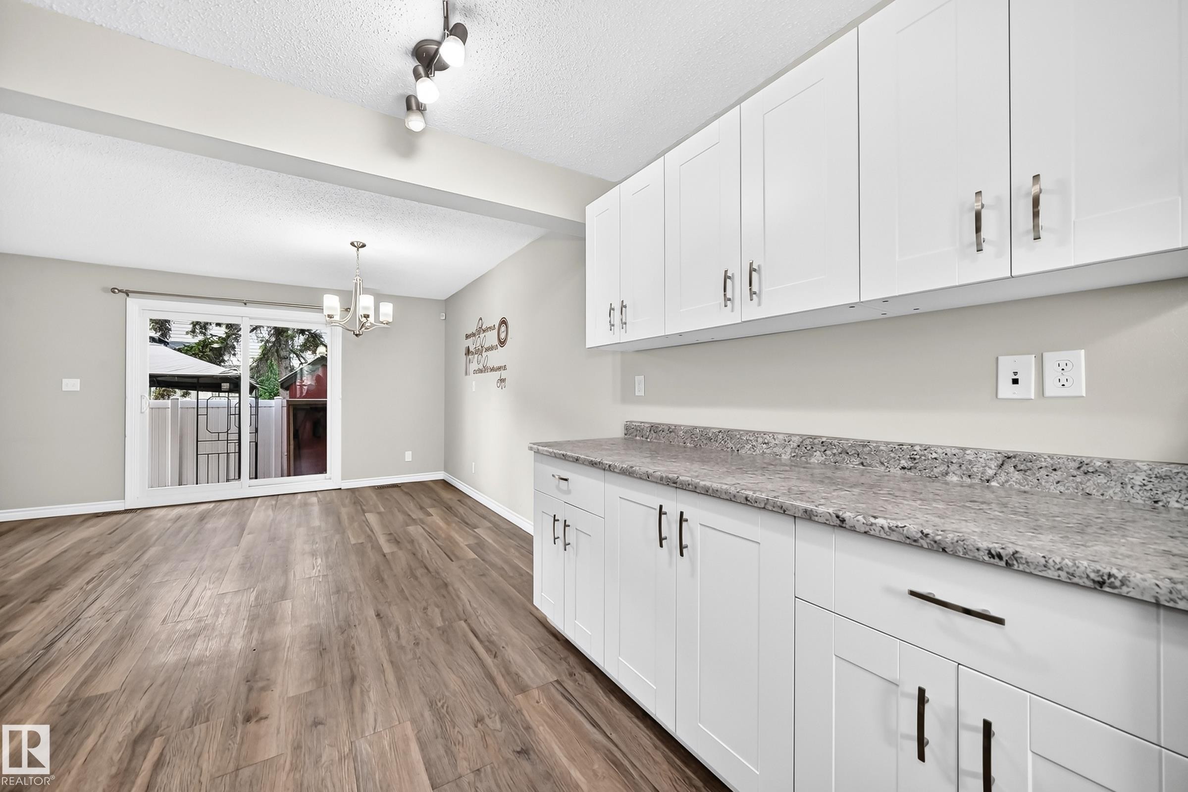 White shaker-style cabinetry with dark hardware, speckled countertops, wood-finish flooring, and a sliding glass door - 18146 81 Avenue Nw, Edmonton, AB