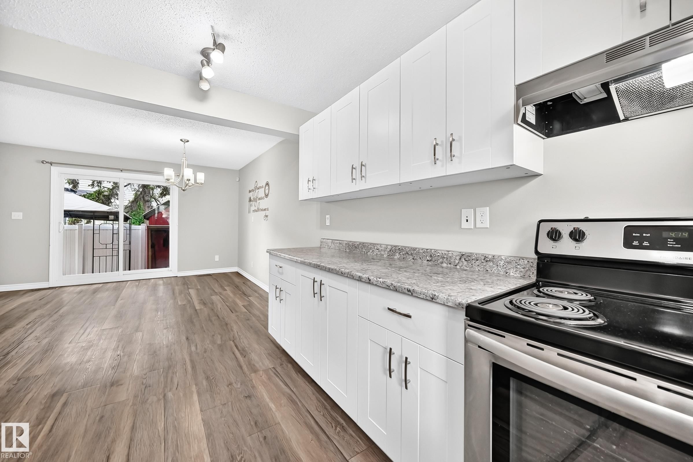White cabinetry with stainless hardware, stone-finish countertops, wood-finish flooring, and a sliding glass door to the exterior - 18146 81 Avenue Nw, Edmonton, AB