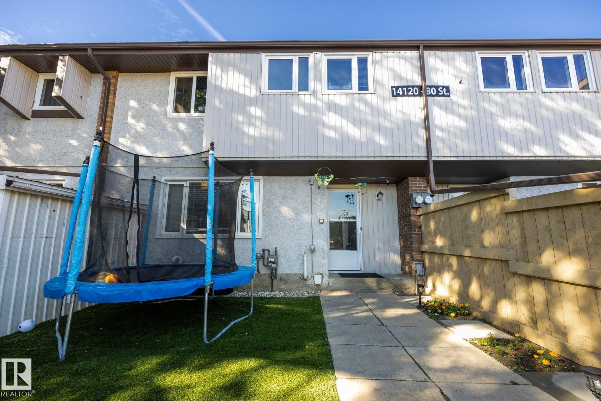 Exterior featuring light-colored siding, a white entry door, and multiple windows - #2 14120 80 St Nw, Edmonton, AB