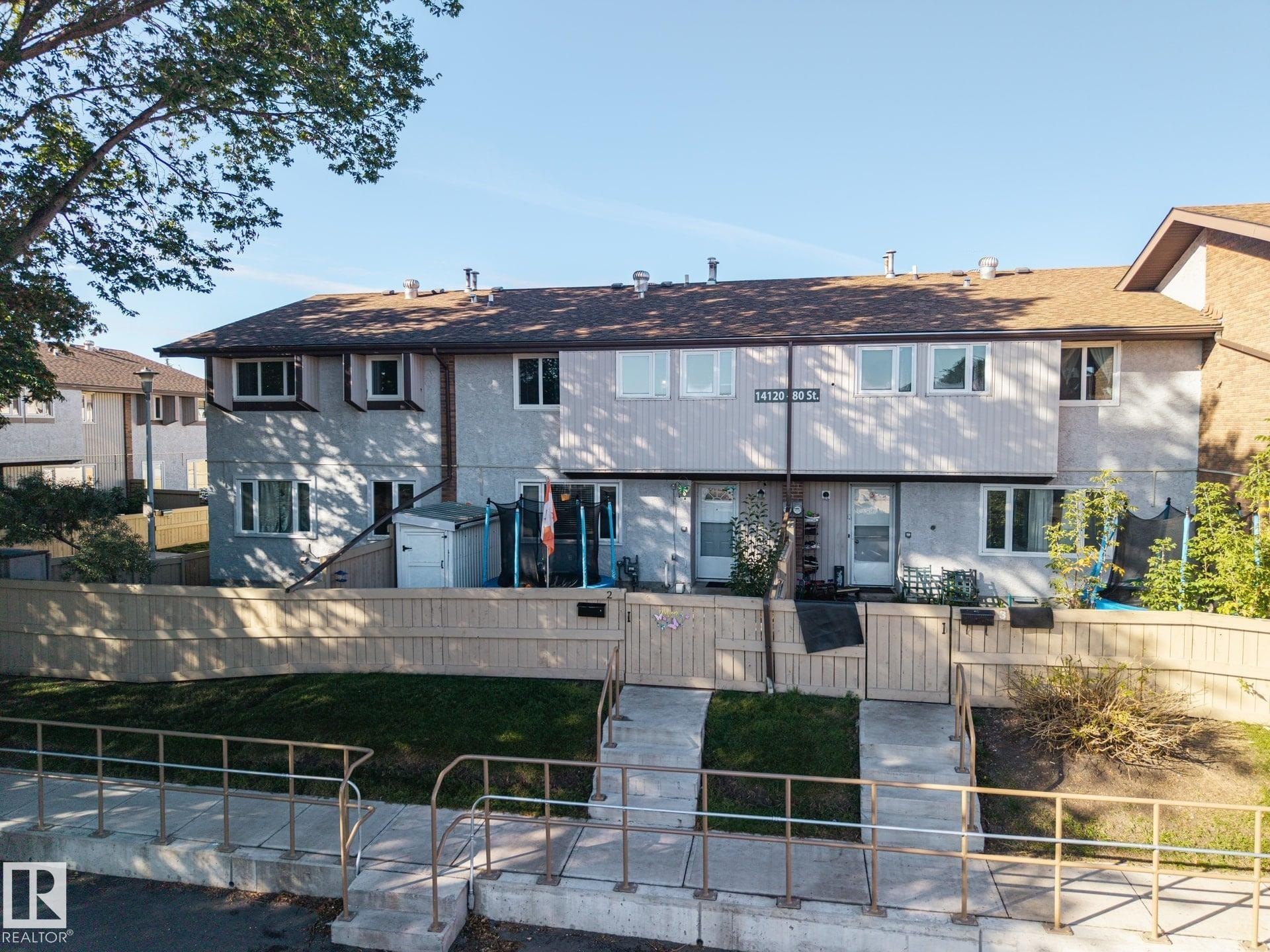 Two-story stucco and siding facade with multiple windows, private fenced yard, and a shingle roof - #2 14120 80 St Nw, Edmonton, AB