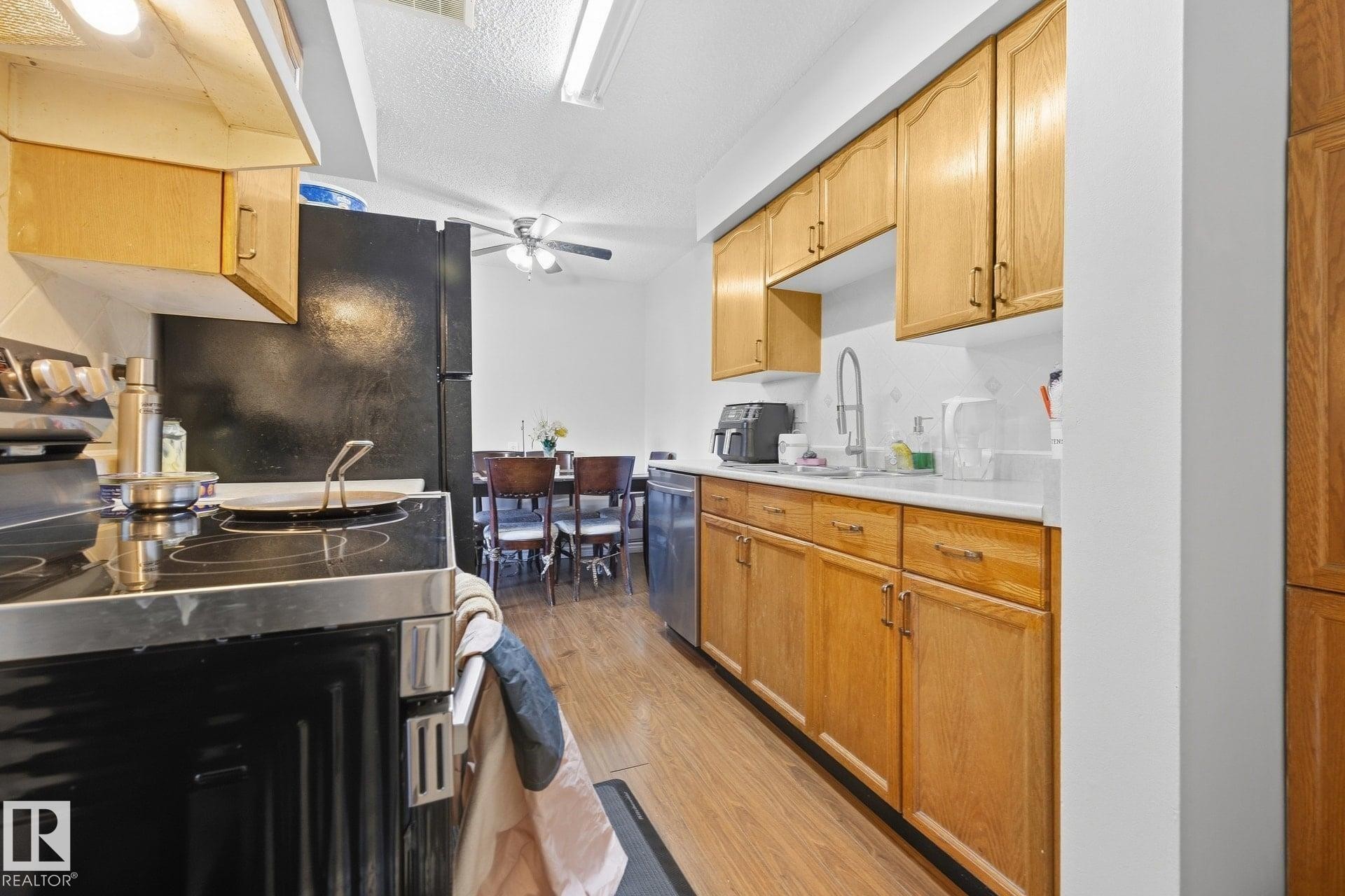 Kitchen featuring wood-finish cabinetry, white countertops, built-in stainless steel dishwasher, and wood-finish flooring - #2 14120 80 St Nw, Edmonton, AB