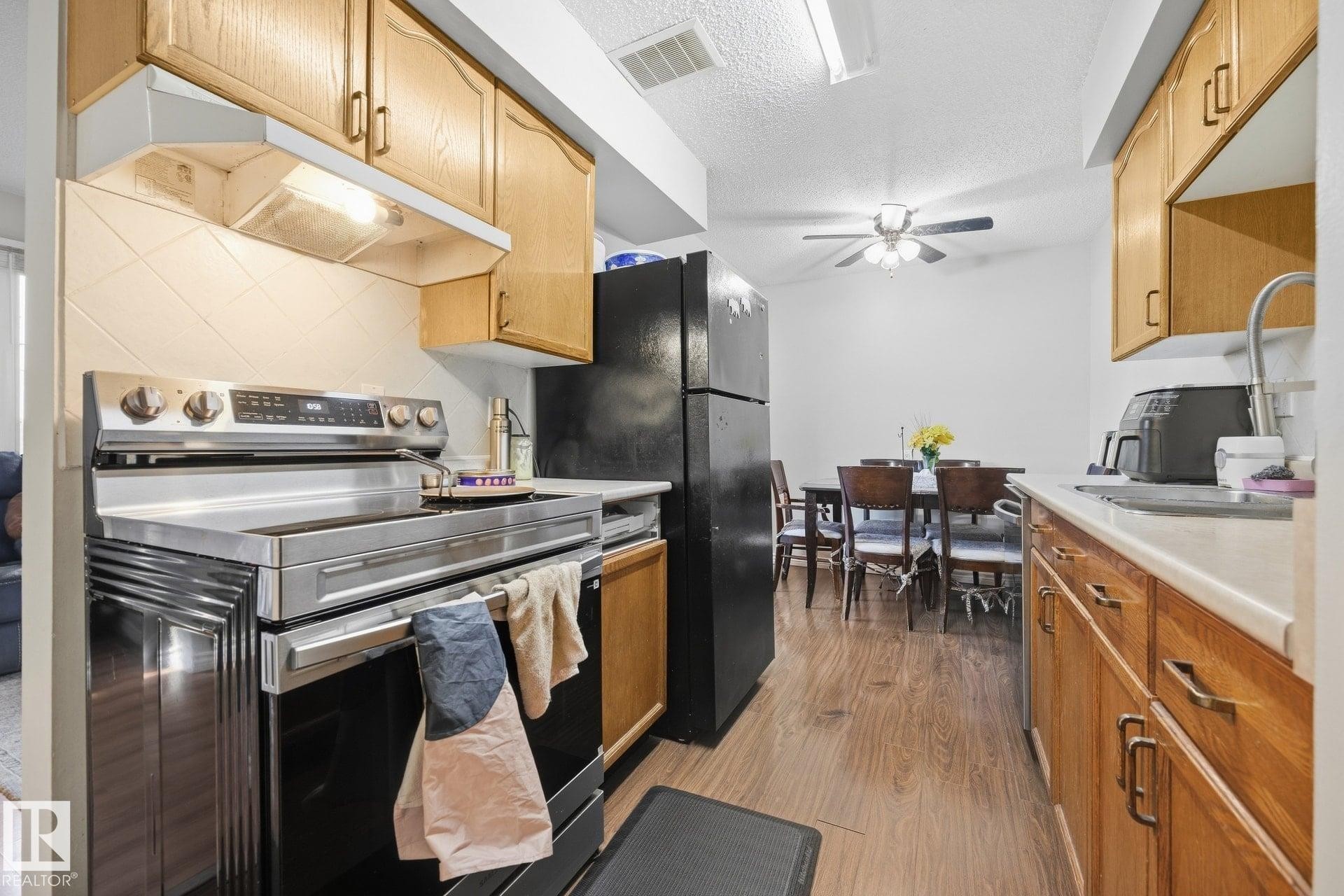 Kitchen featuring a stainless steel range, black refrigerator, wood-finish flooring, and natural wood cabinetry with metal hardware - #2 14120 80 St Nw, Edmonton, AB