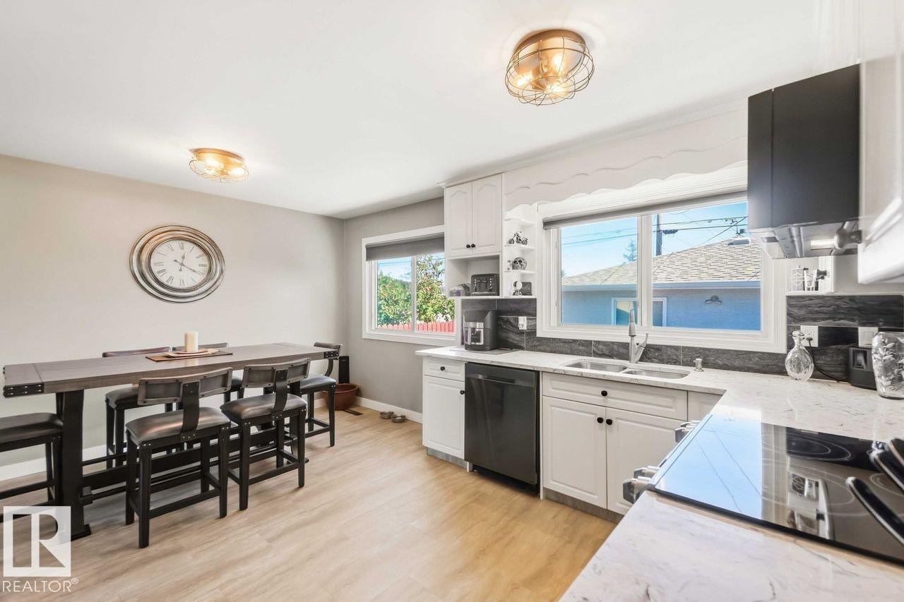 Light wood-finish flooring, white cabinetry, dark stone countertops, stainless steel sink, and modern ceiling light fixtures - 13427 83 Street Nw, Edmonton, AB