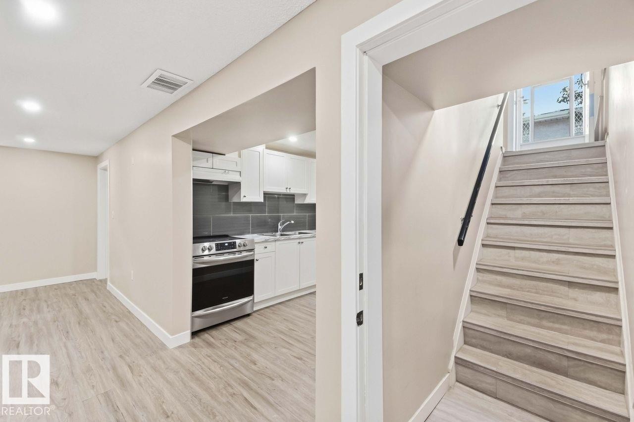 Contemporary kitchen featuring white cabinetry, stainless steel range, gray tile backsplash, and light wood-finish flooring - 13427 83 Street Nw, Edmonton, AB