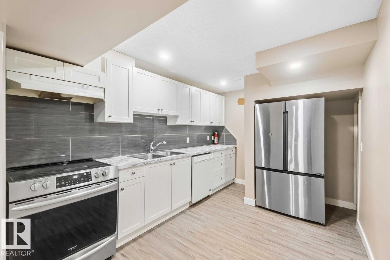 Stainless steel appliances, white cabinetry, grey subway tile backsplash, light wood-finish flooring, and recessed lighting - 13427 83 Street Nw, Edmonton, AB