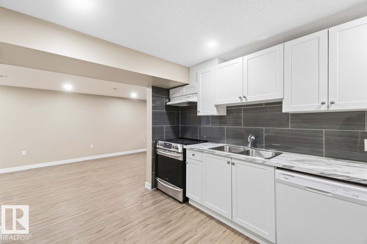 White cabinetry with stainless steel hardware, wood-finish flooring, recessed lighting, and a dark tile backsplash - 13427 83 Street Nw, Edmonton, AB