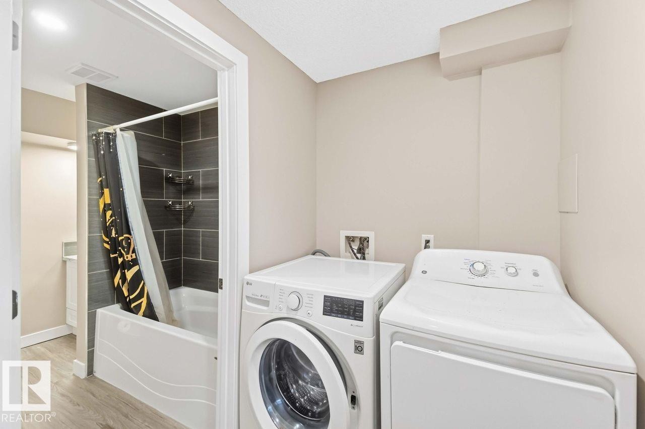 Full-size laundry appliances, a white soaking tub, and dark gray tile shower surround - 13427 83 Street Nw, Edmonton, AB