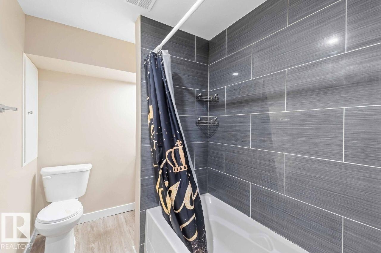 Bathtub with full-height gray wall tile surround and a toilet - 13427 83 Street Nw, Edmonton, AB