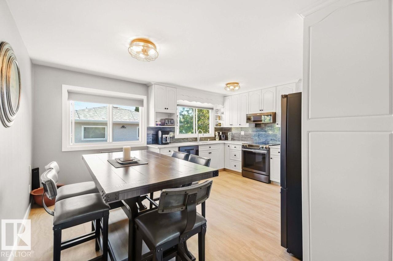 Light wood-finish flooring, white cabinetry, dark-finish appliances, light-toned countertops, and a tile backsplash - 13427 83 Street Nw, Edmonton, AB