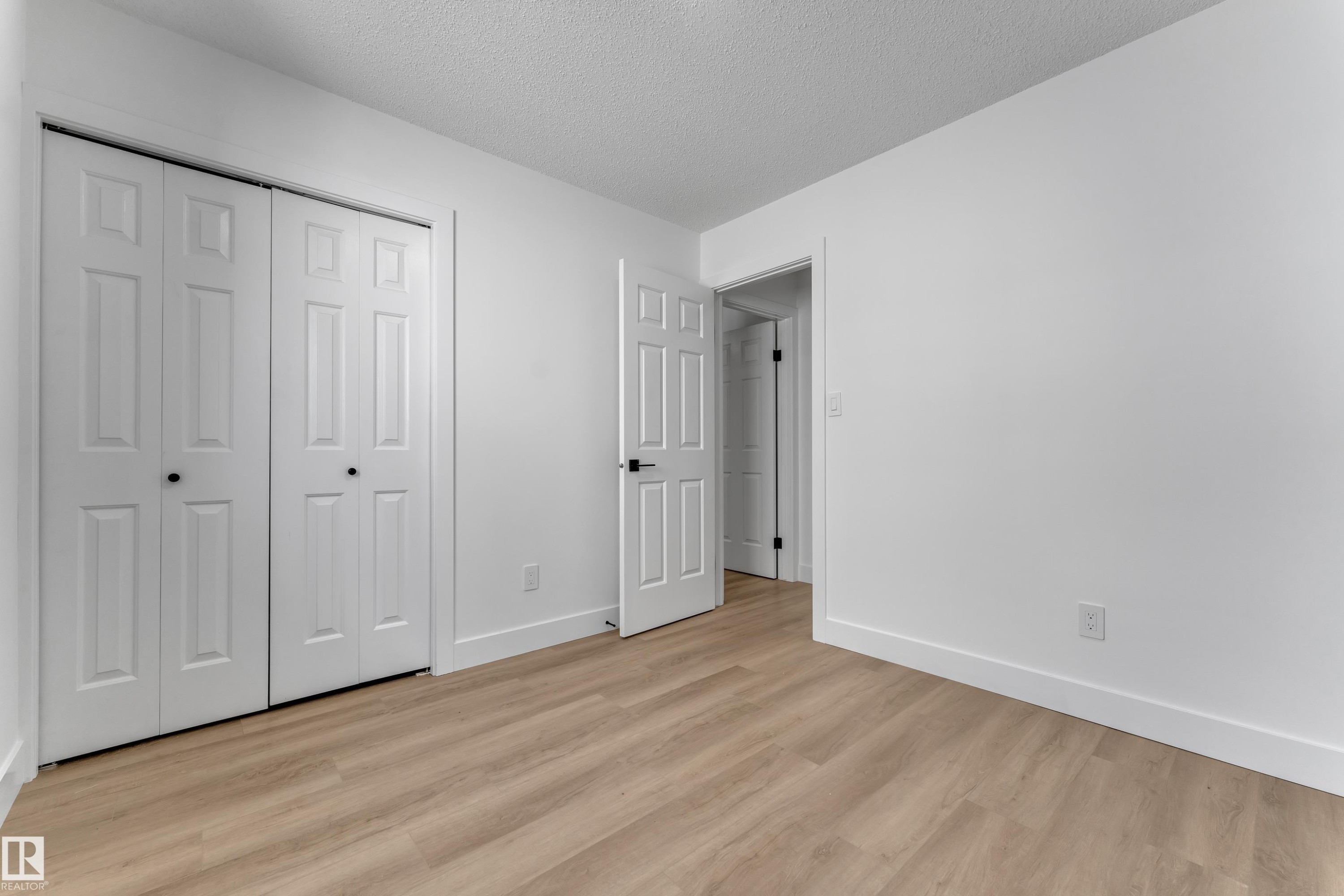 Wood-finish flooring, white walls, white bi-fold closet doors, and contrasting dark hardware - 3320 43 Street Nw, Edmonton, AB