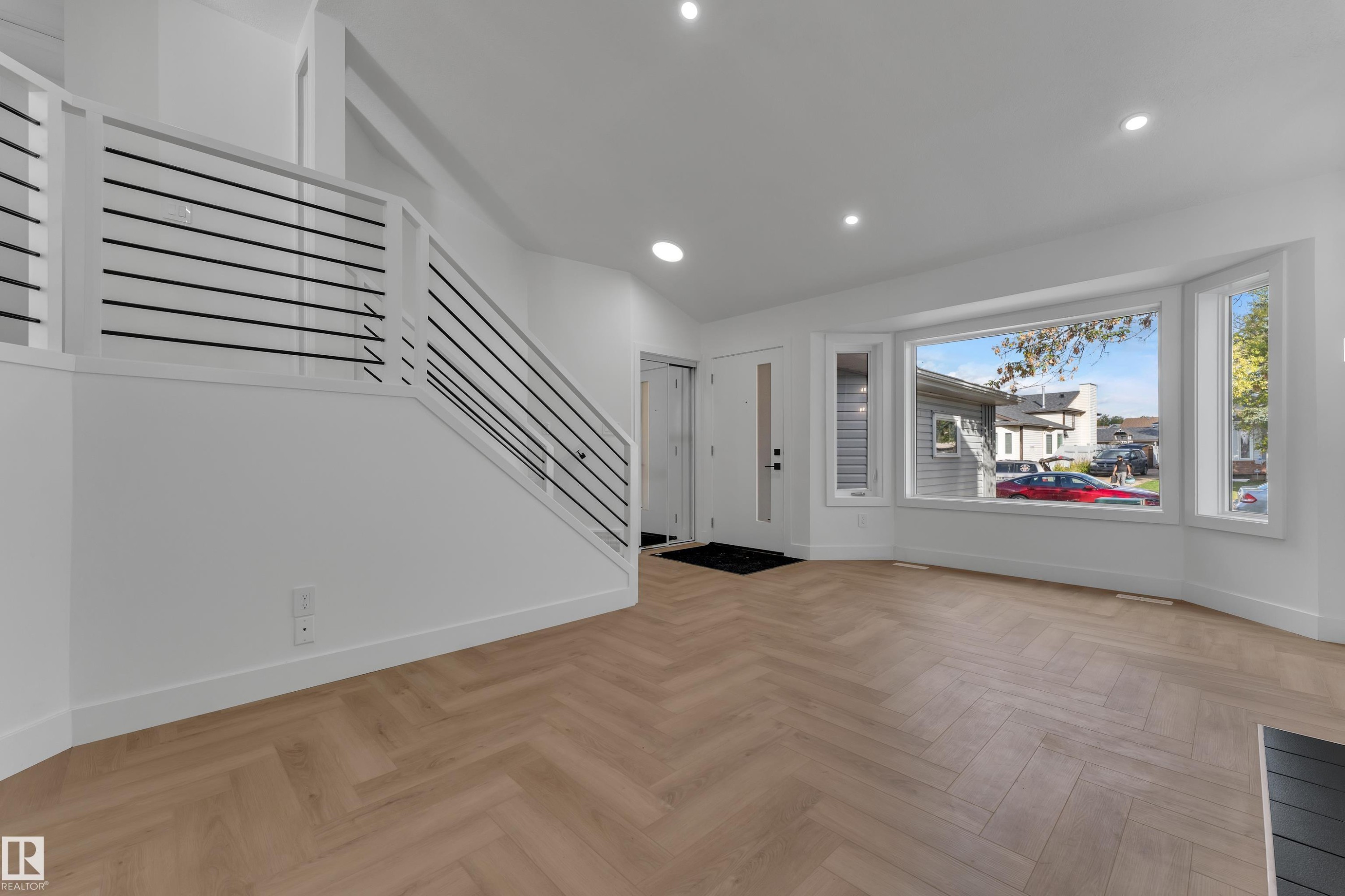 Herringbone wood-finish flooring, contemporary staircase with horizontal metal balusters, recessed lighting, and a bay window - 3320 43 Street Nw, Edmonton, AB