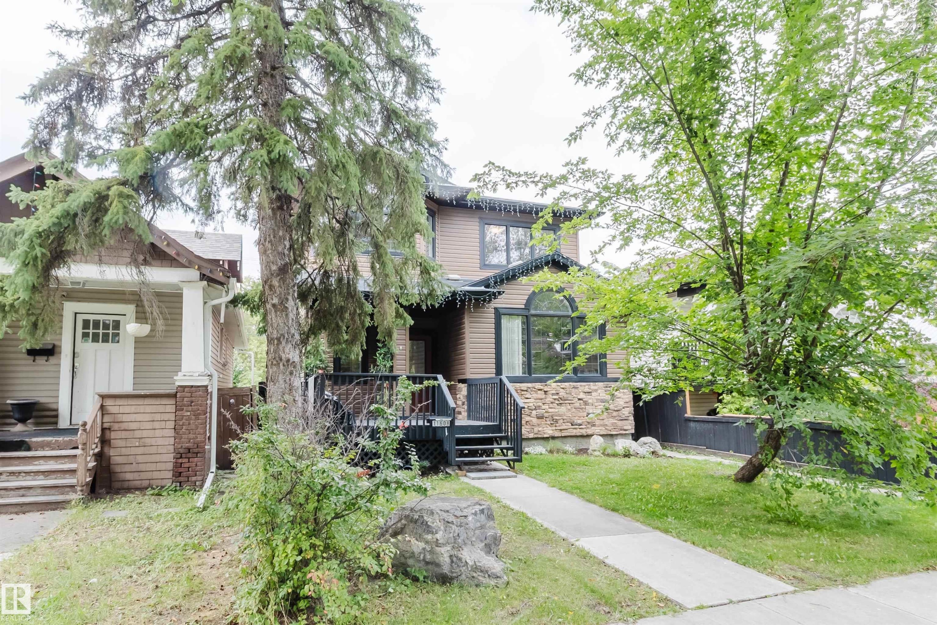 Two-story exterior with siding and stone accents, featuring a prominent arched window and an elevated deck with dark railings - 11608 96 Street Nw, Edmonton, AB
