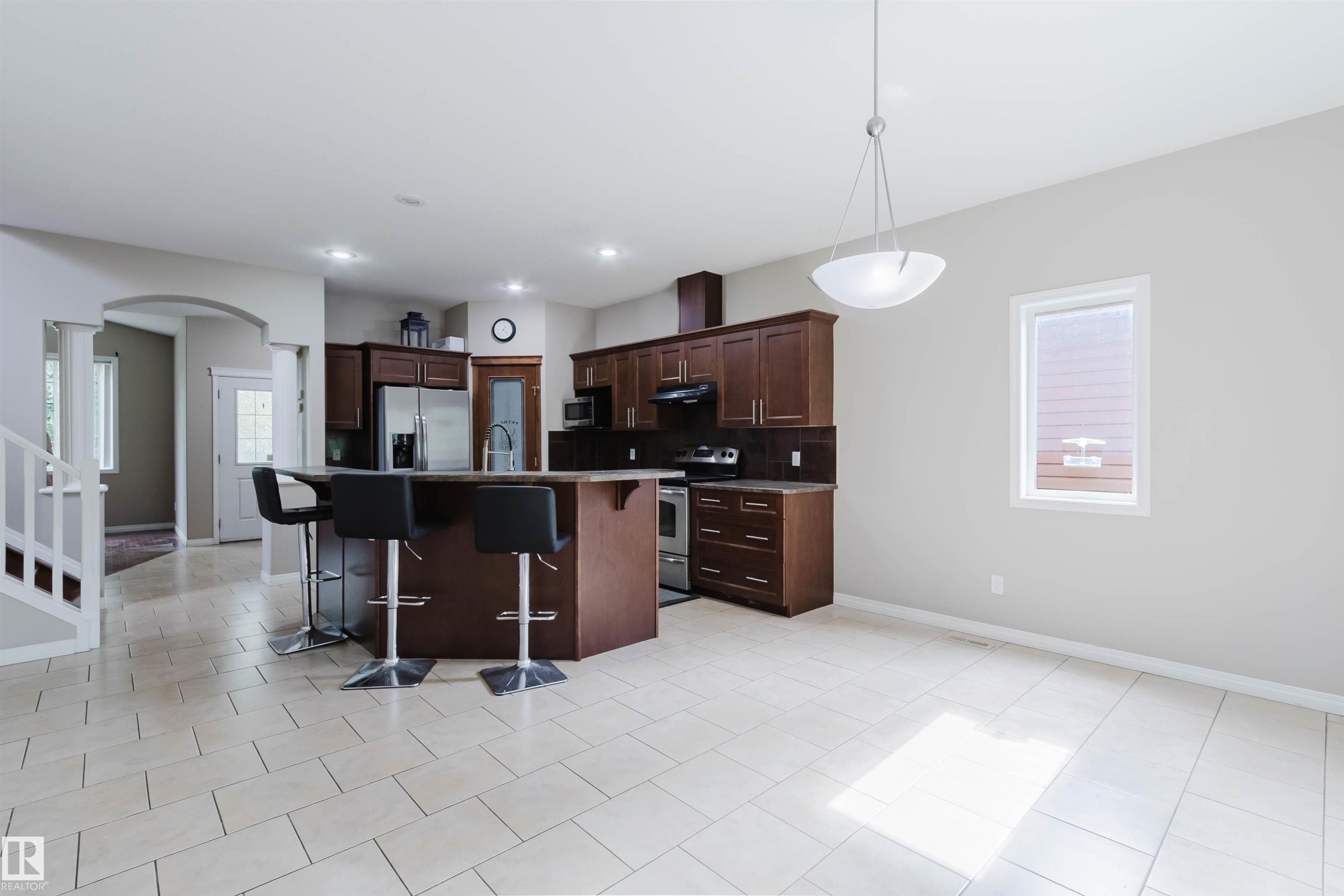 Kitchen featuring dark wood cabinetry, stainless steel appliances, a center island with bar seating, and tile flooring - 11608 96 Street Nw, Edmonton, AB