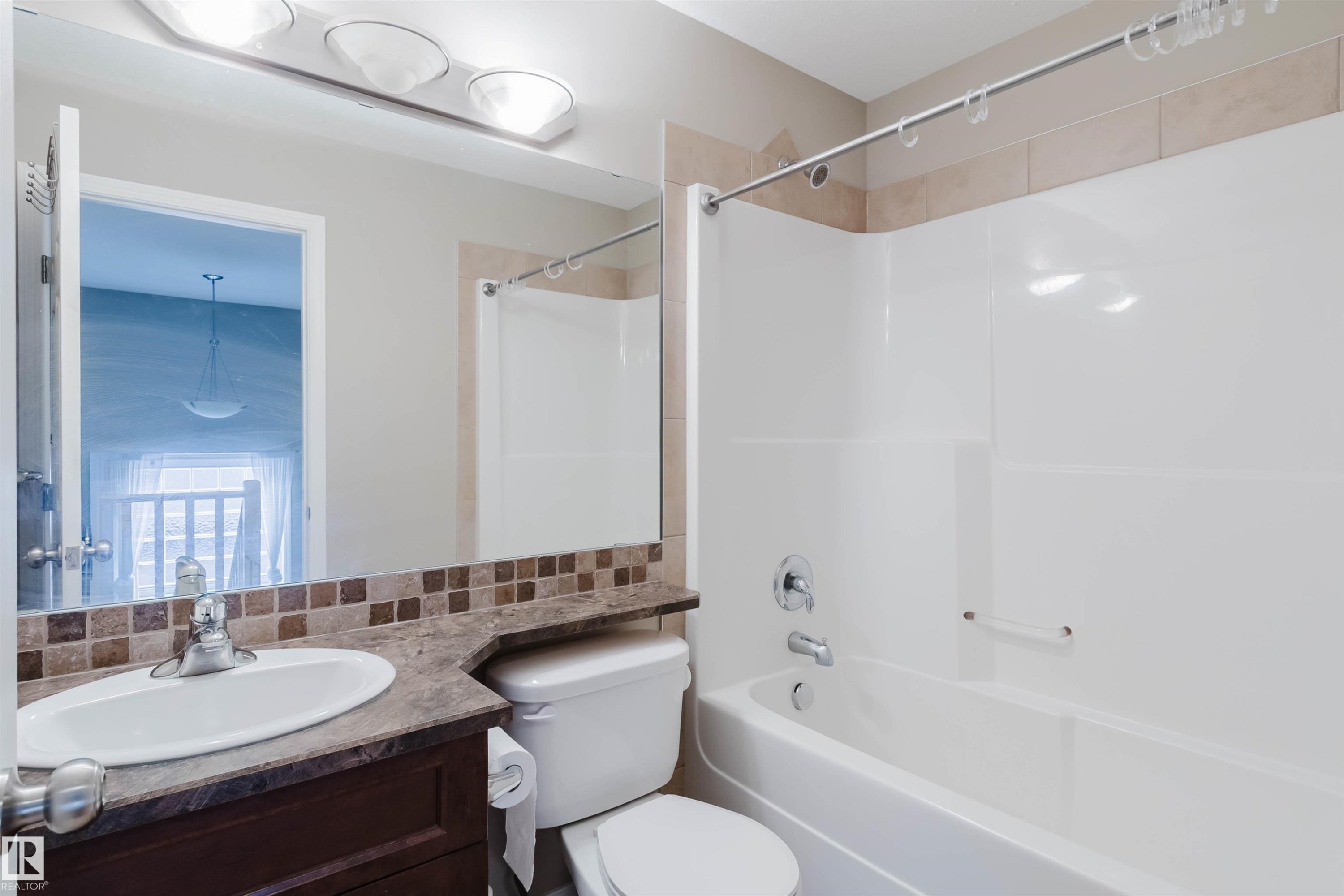 Tub/shower combination with chrome fixtures, vanity with integrated sink, patterned tile backsplash, and overhead lighting - 11608 96 Street Nw, Edmonton, AB