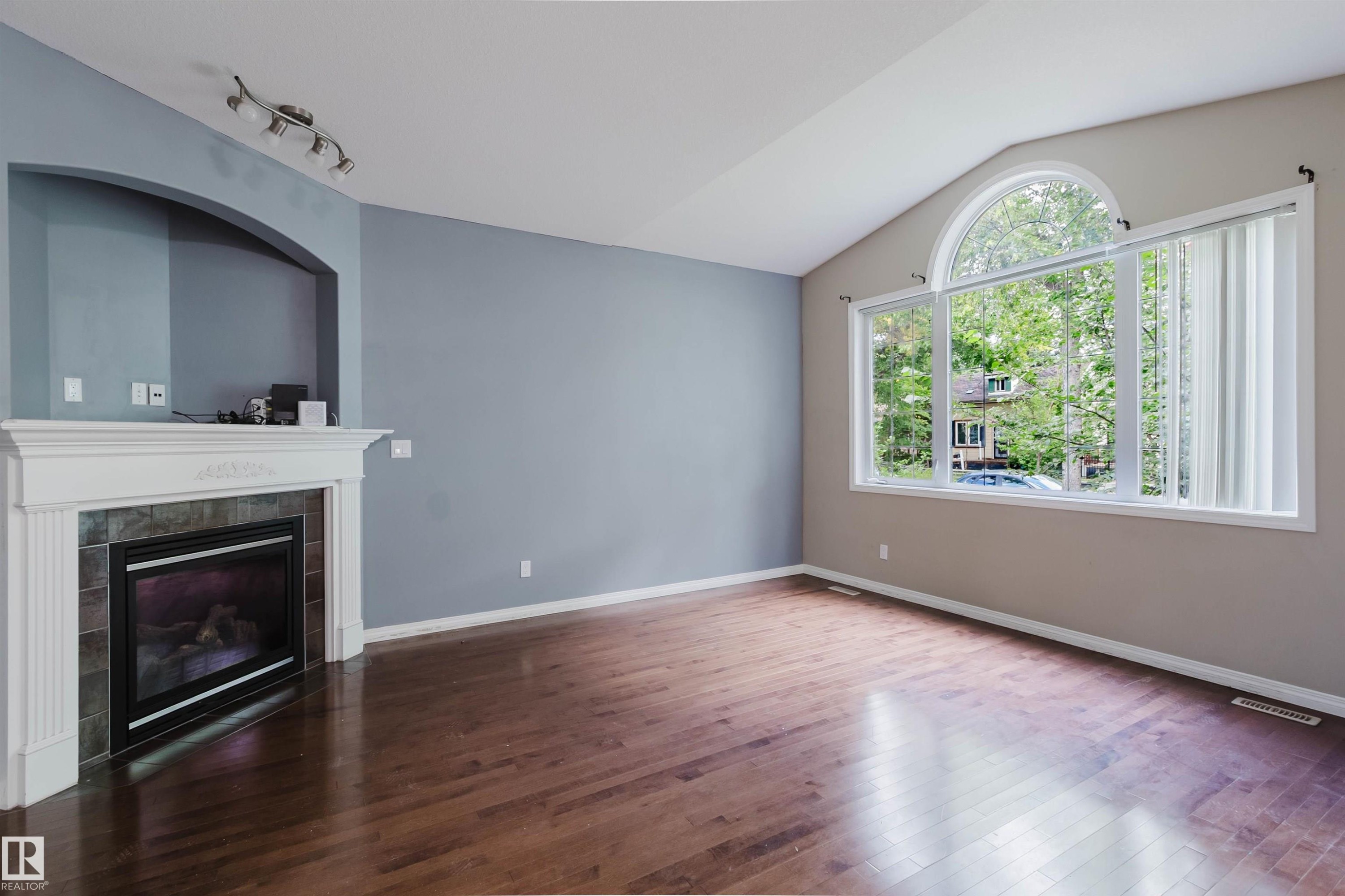 Vaulted ceiling, wood-finish flooring, fireplace with tile surround, arched alcove, and large arched window - 11608 96 Street Nw, Edmonton, AB