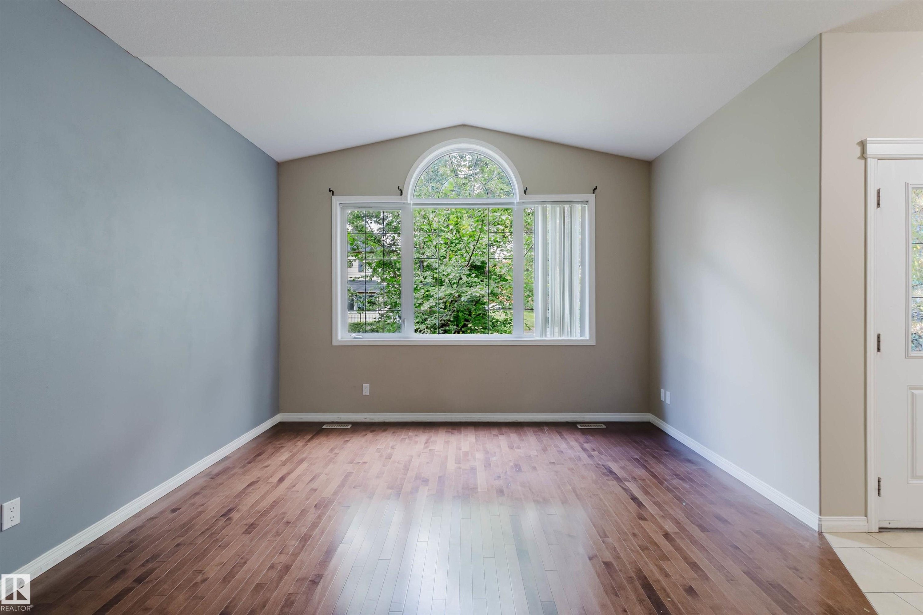 Vaulted ceiling with an arched transom window, wood-finish flooring, and a paneled entry door with frosted glass - 11608 96 Street Nw, Edmonton, AB