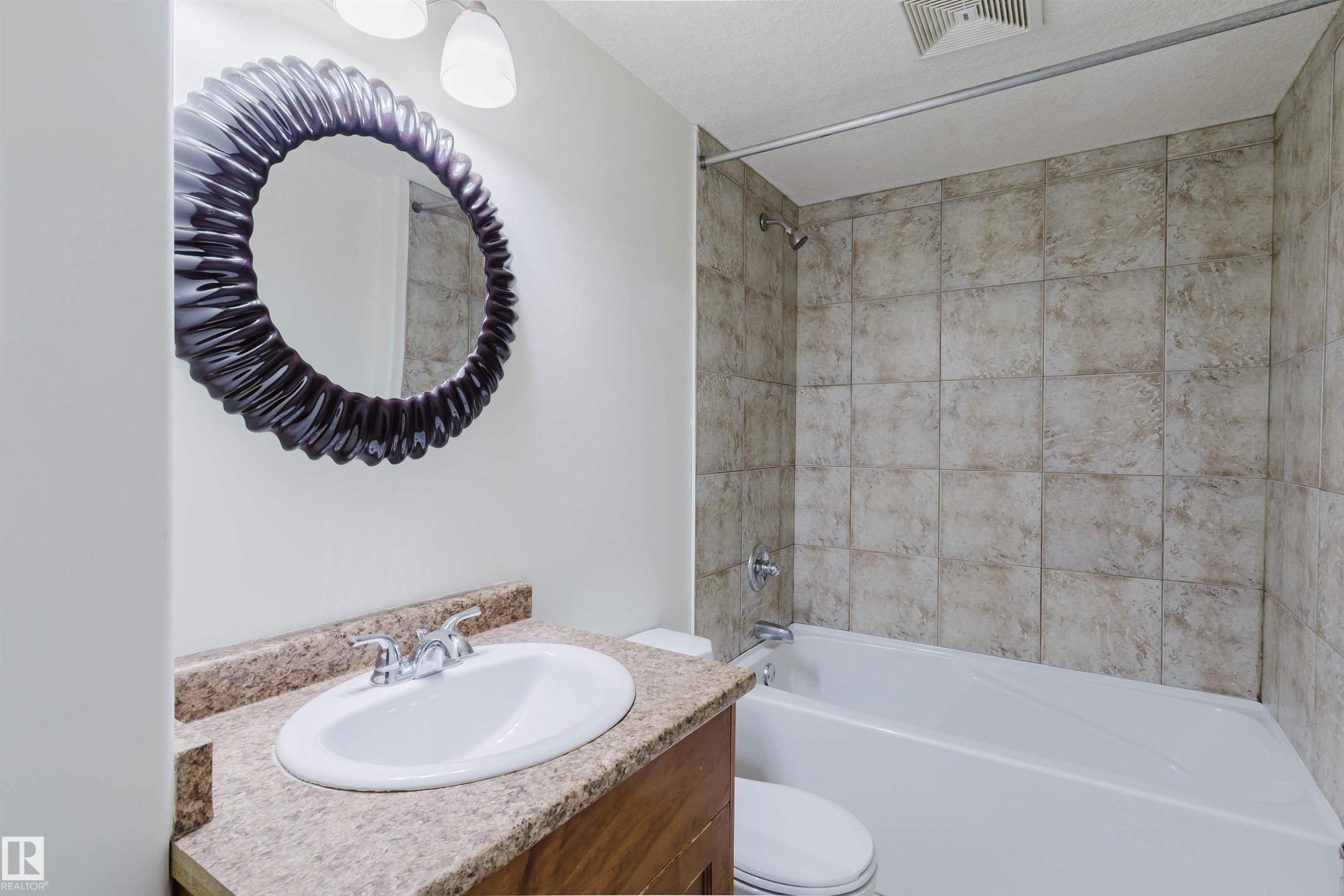 Bathroom featuring a vanity with an integrated sink, a speckled countertop, and a tiled shower/tub combination - 11608 96 Street Nw, Edmonton, AB