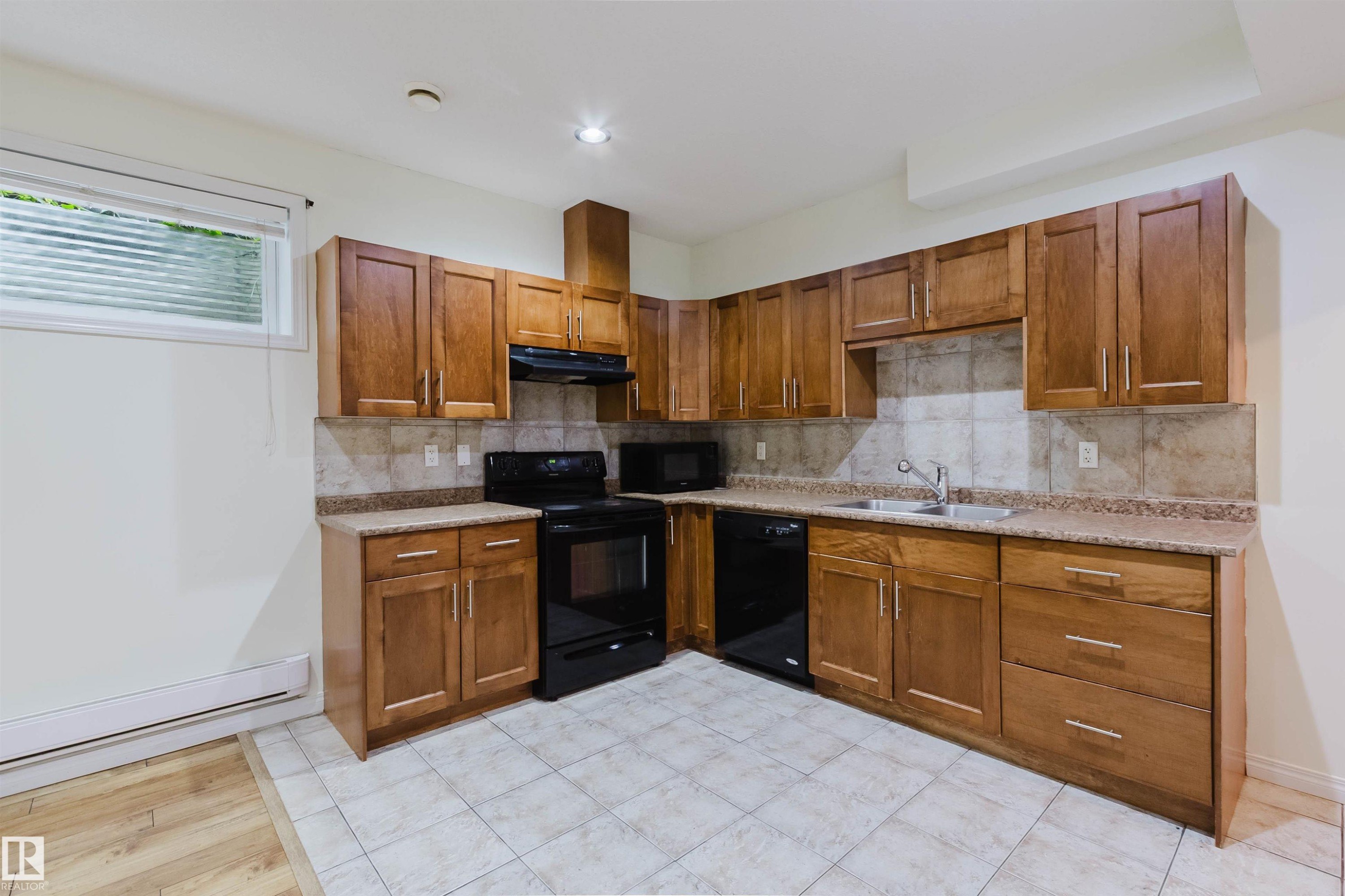 Kitchen featuring wood-finish cabinetry, tile backsplash, black appliances, and durable tile flooring - 11608 96 Street Nw, Edmonton, AB