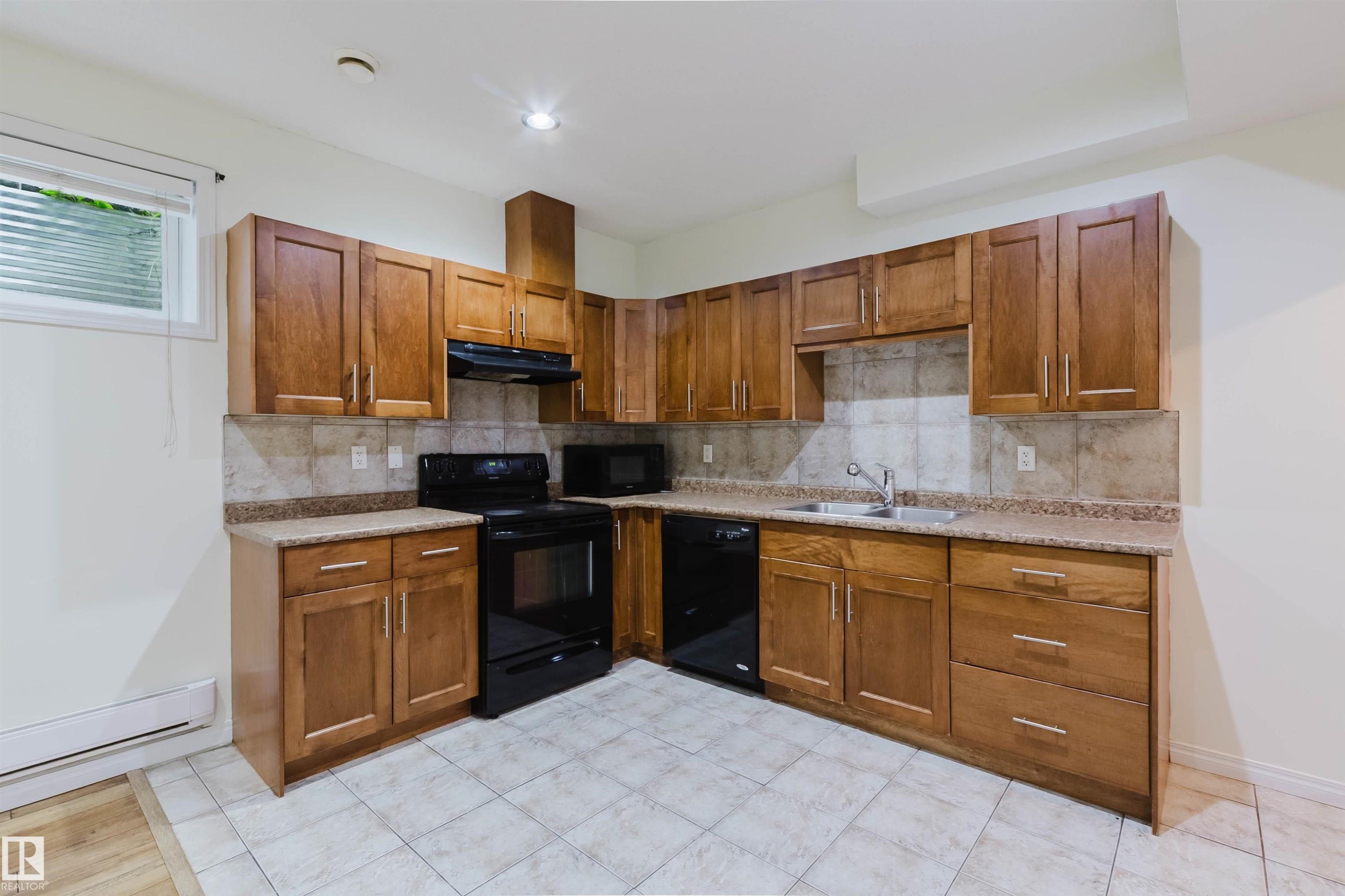 Wood-finish cabinetry with silver-tone hardware, speckled countertops, tile backsplash, and black appliances - 11608 96 Street Nw, Edmonton, AB
