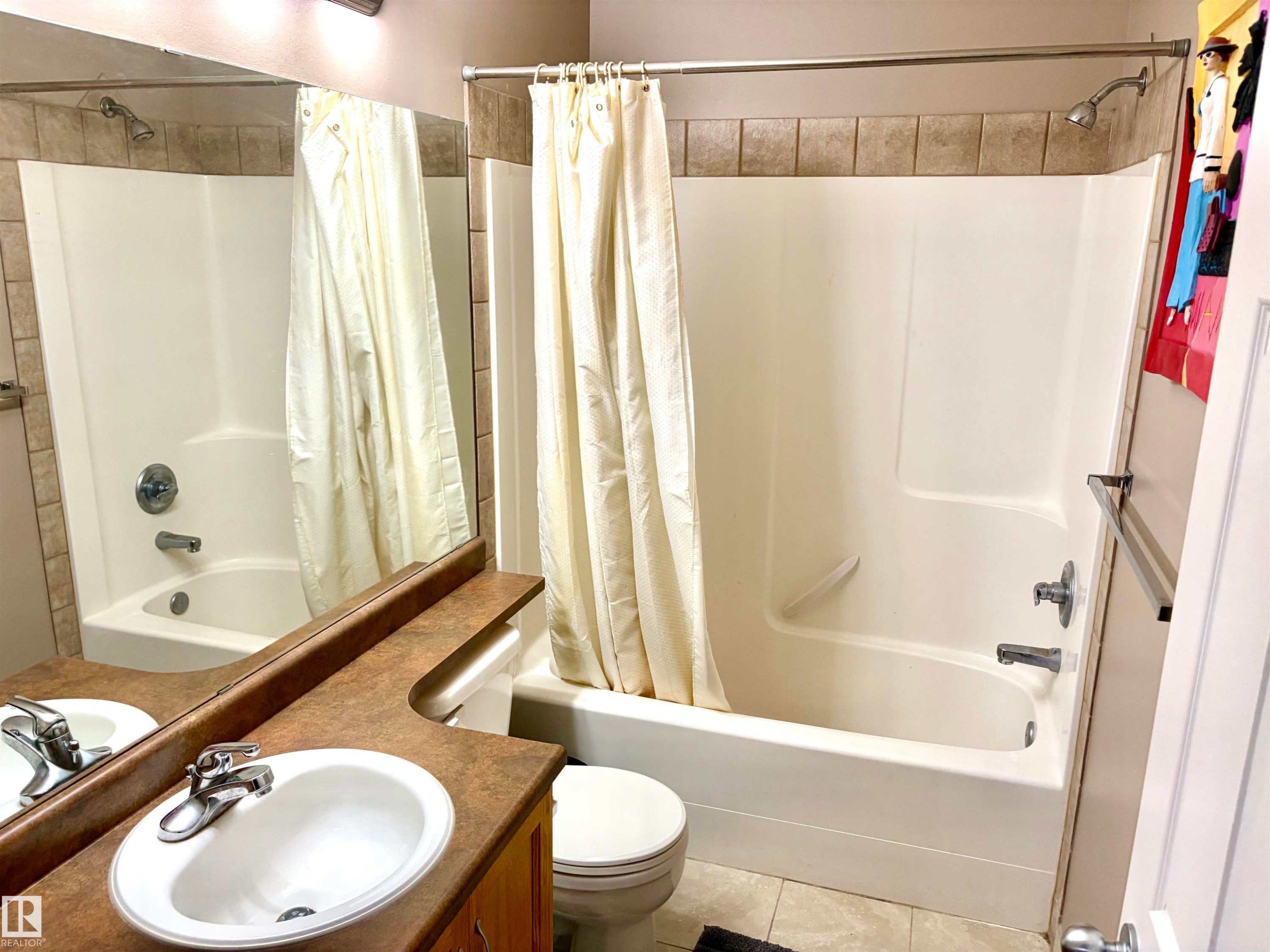 Bathtub and shower combination with a tiled surround, a toilet, a vanity with a surface-mounted sink, and a mirrored wall - #17 16317 64 St Nw, Edmonton, AB