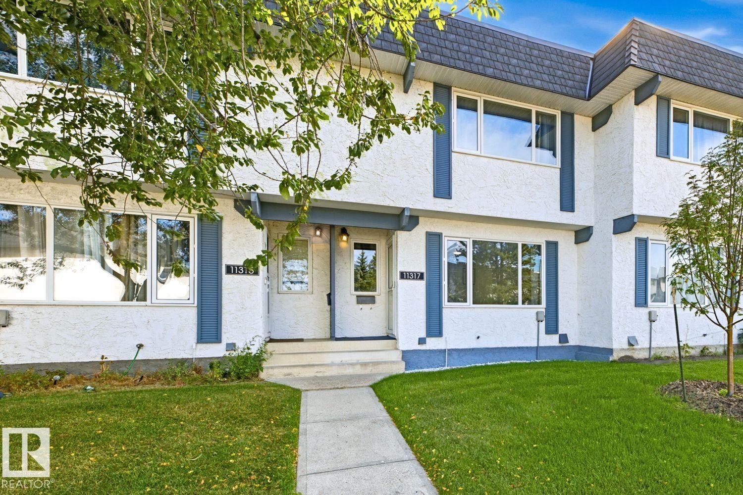 Stucco exterior with blue trim accents, asphalt shingle roofing, ground-level windows, and a concrete walkway - 11317 22 Avenue Nw, Edmonton, AB