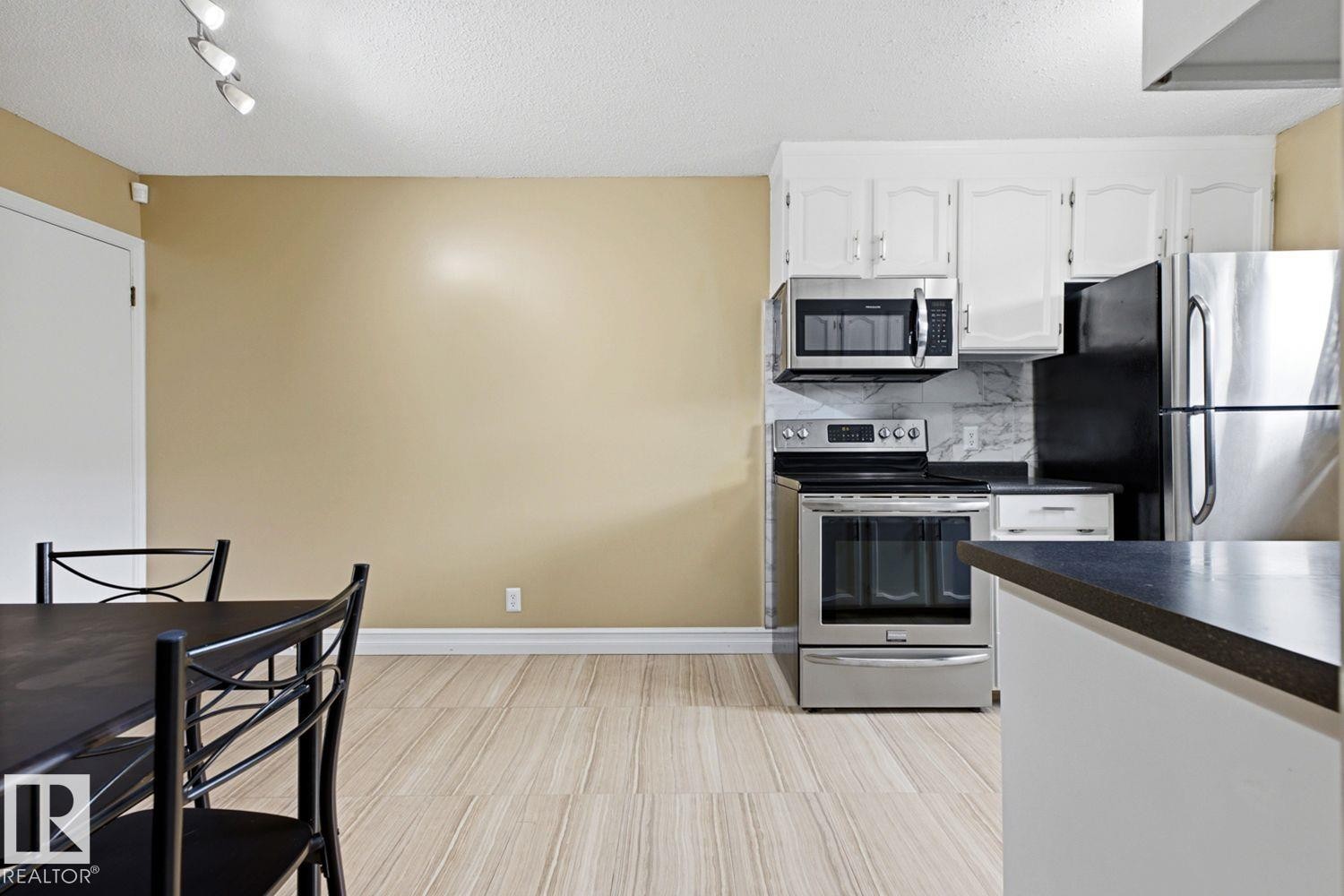 Kitchen featuring stainless steel appliances, white cabinetry, dark countertops, and a tiled backsplash - 11317 22 Avenue Nw, Edmonton, AB
